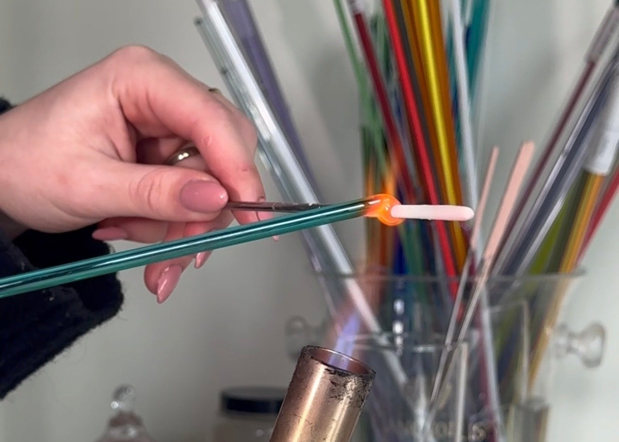 Person holding a colorful straw with a flame at the end, surrounded by various straws.