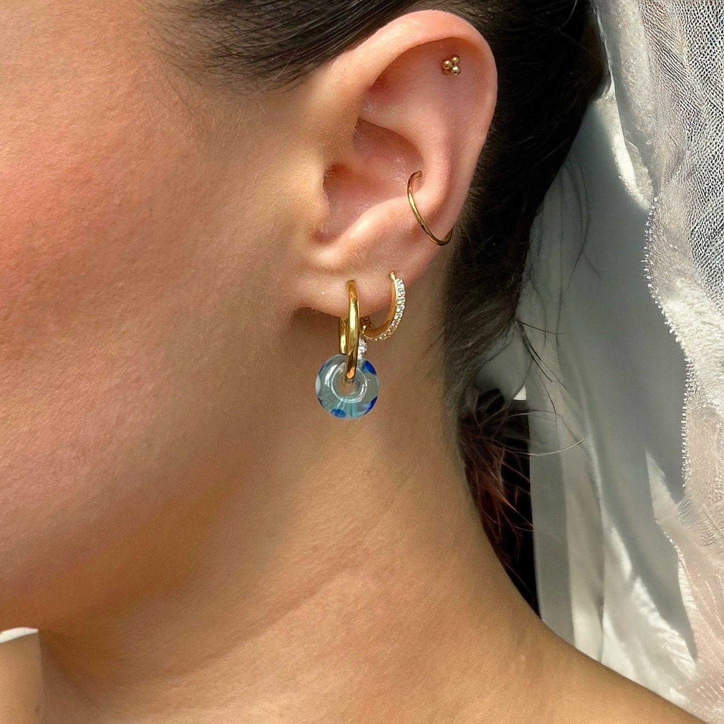 
                  
                    Close-up of an ear wearing gold hoop earrings with a blue stone.
                  
                