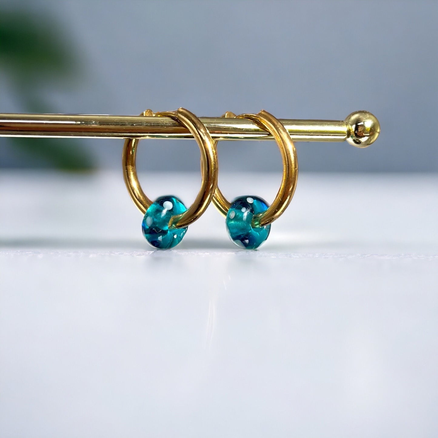 
                  
                    Gold hoop earrings with blue beads on a light gray background
                  
                