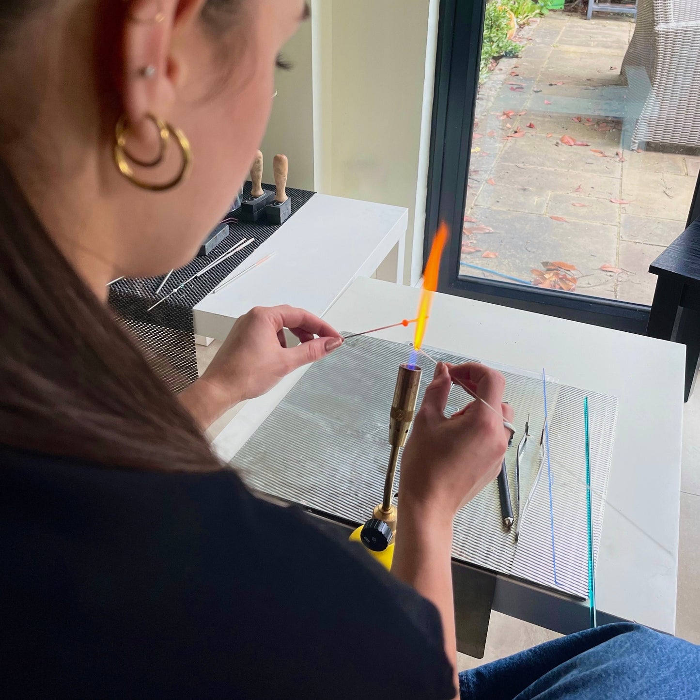 
                  
                    Person using a torch to work on a glass surface with a view of a patio outside.
                  
                