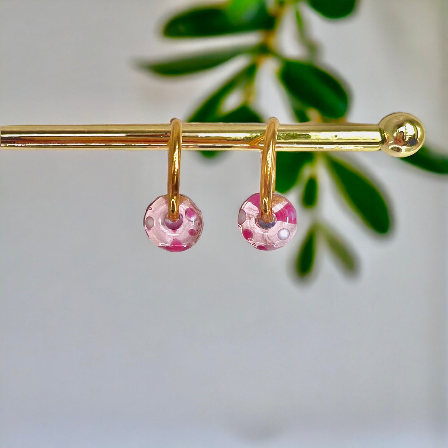 Gold earring with pink beads on a blurred green leaf background