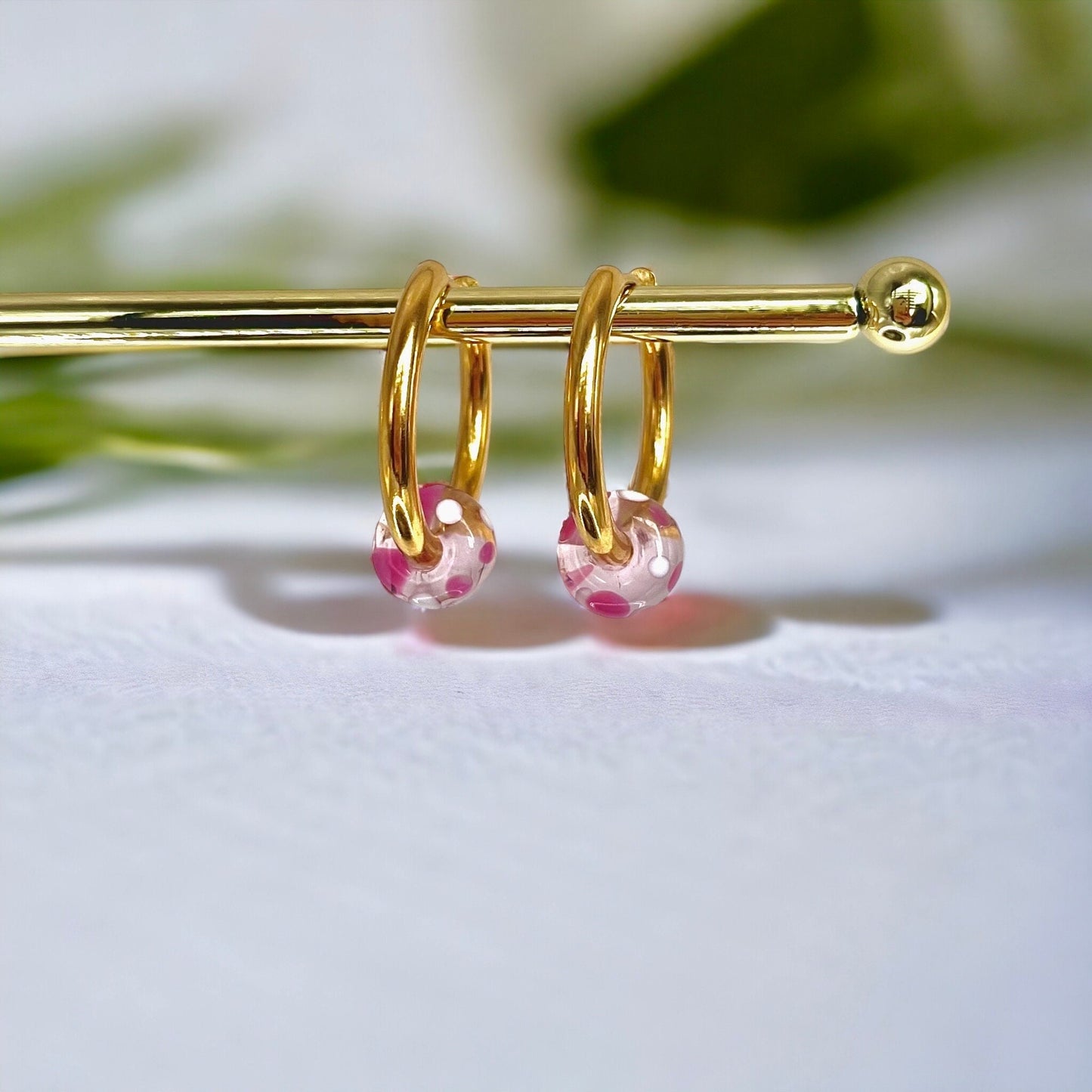 
                  
                    Gold hoop earrings with pink beads on a white background
                  
                