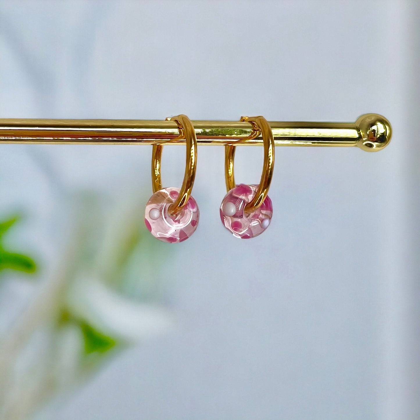 Gold hoop earrings with pink beads on a gold rod against a blurred natural background