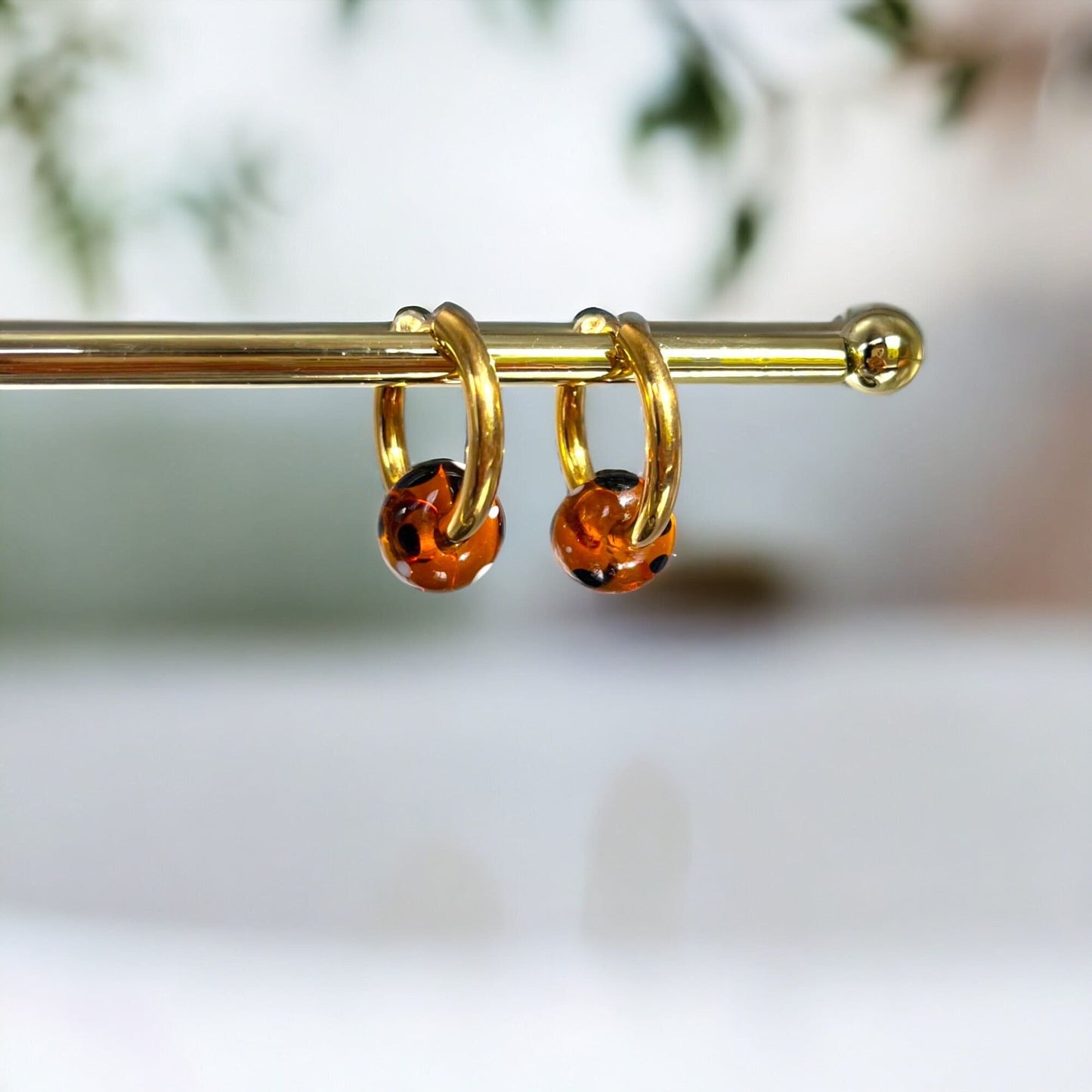 Gold hoop earrings with orange gemstones on a blurred natural background