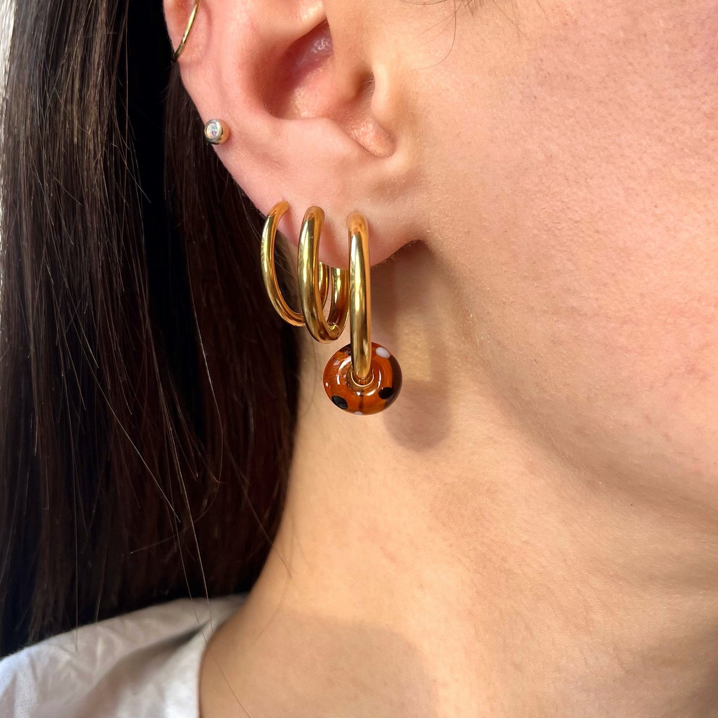 
                  
                    Close-up of a person wearing gold hoop earrings with a dark background
                  
                