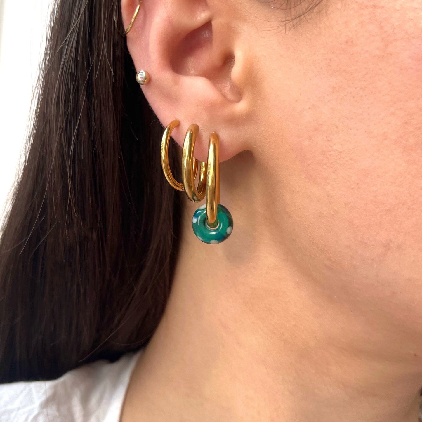 
                  
                    Gold hoop earrings with a blue center worn by a person.
                  
                