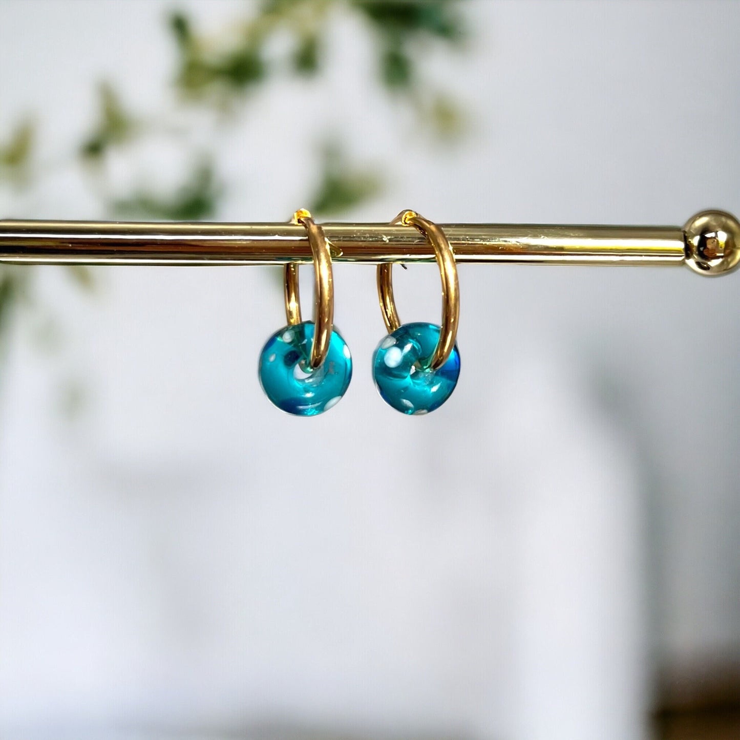 Gold hoop earrings with blue beads on a blurred natural background
