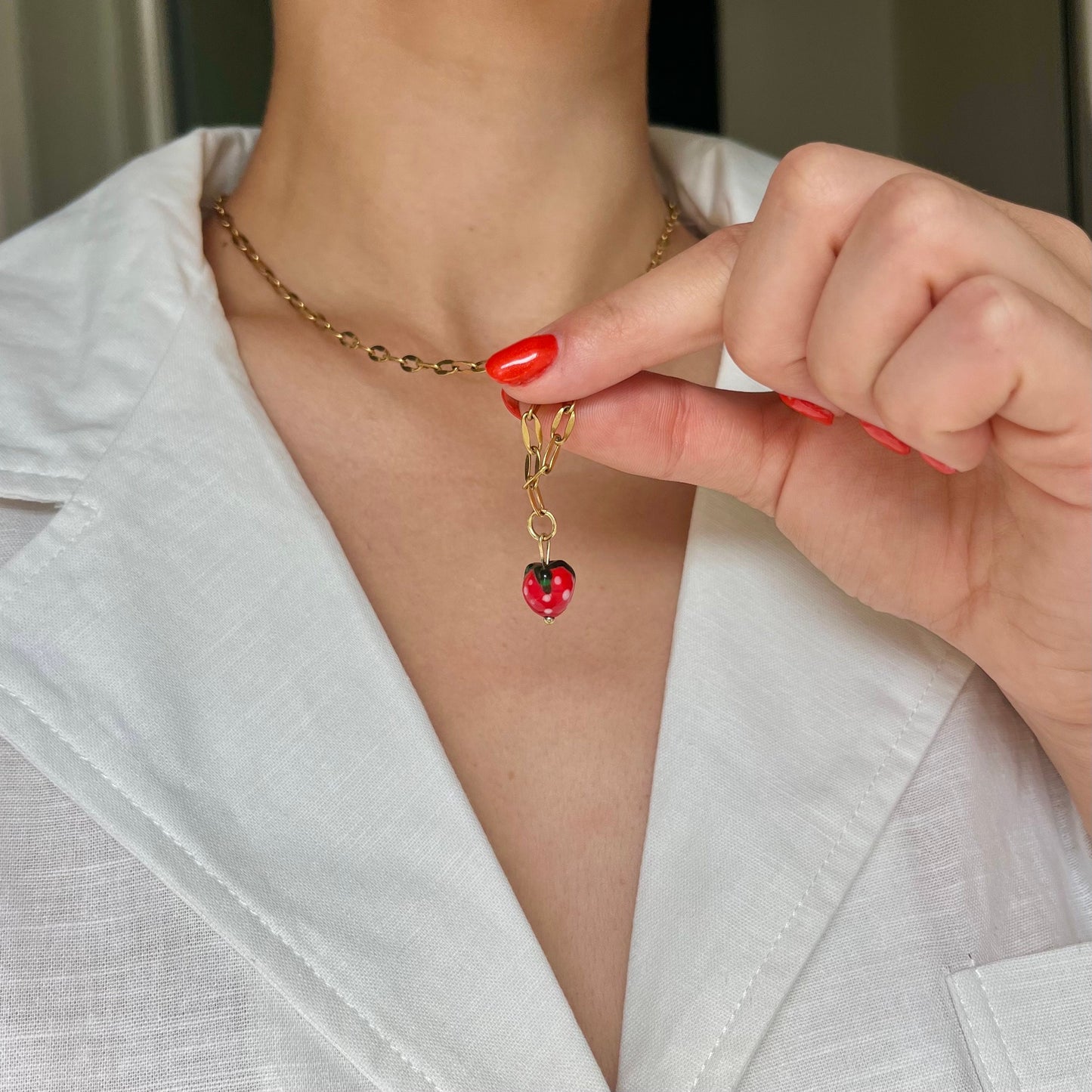 
                  
                    Gold necklace with a red pendant being adjusted on a person wearing a white blazer.
                  
                