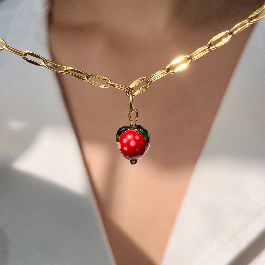 Gold chain necklace with a red berry pendant on a blurred background