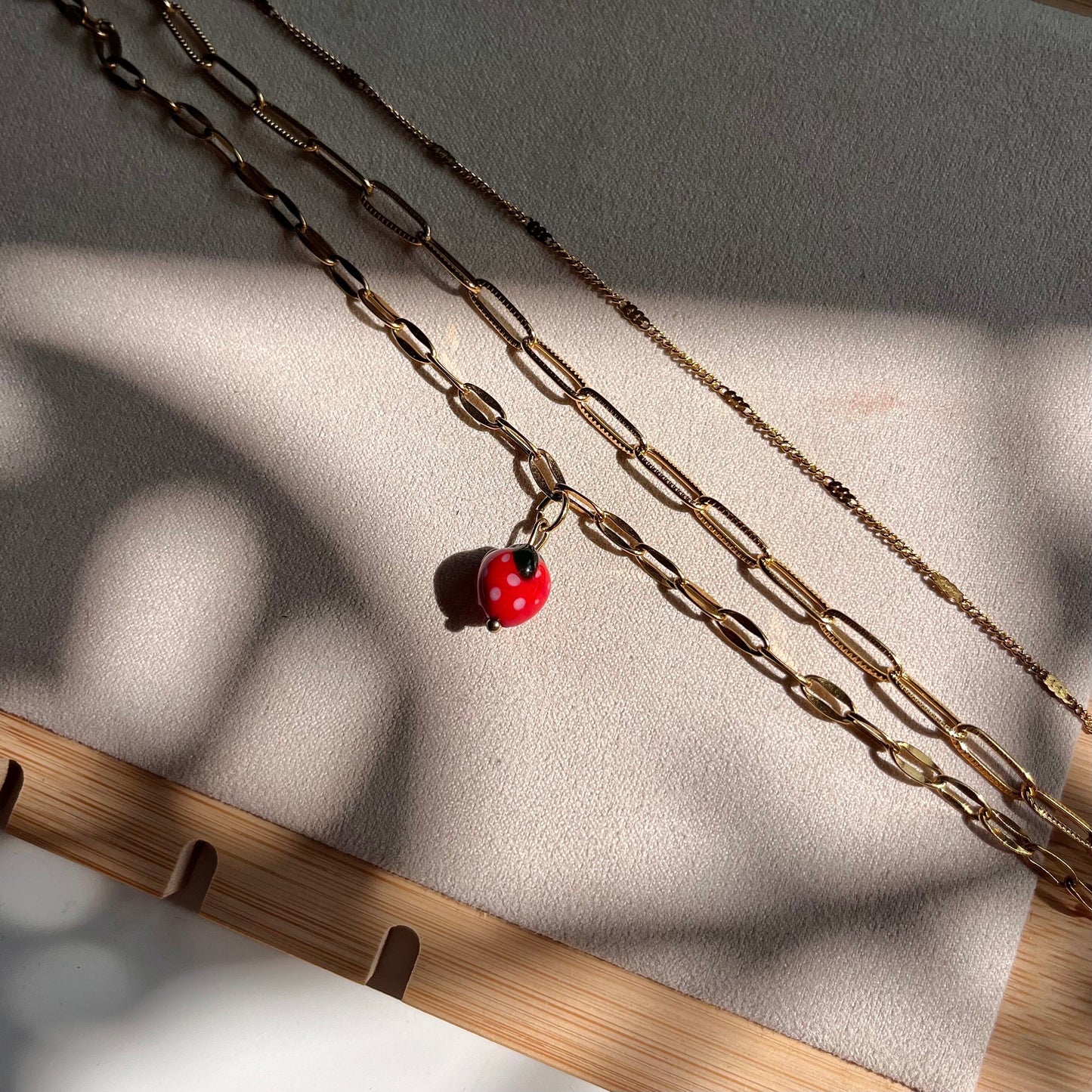 
                  
                    Two gold chain necklaces with a red pendant on a textured surface.
                  
                