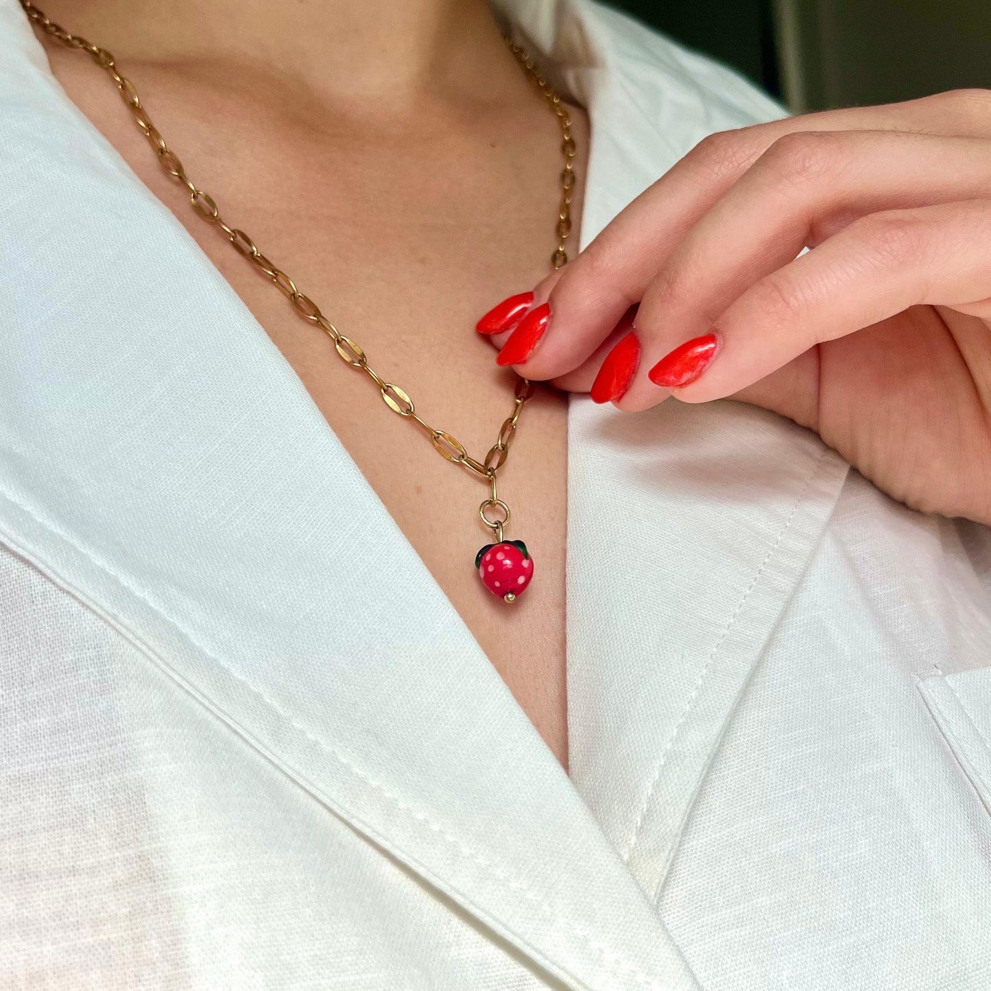 Gold necklace with a red pendant worn by a person with red nail polish on a white background