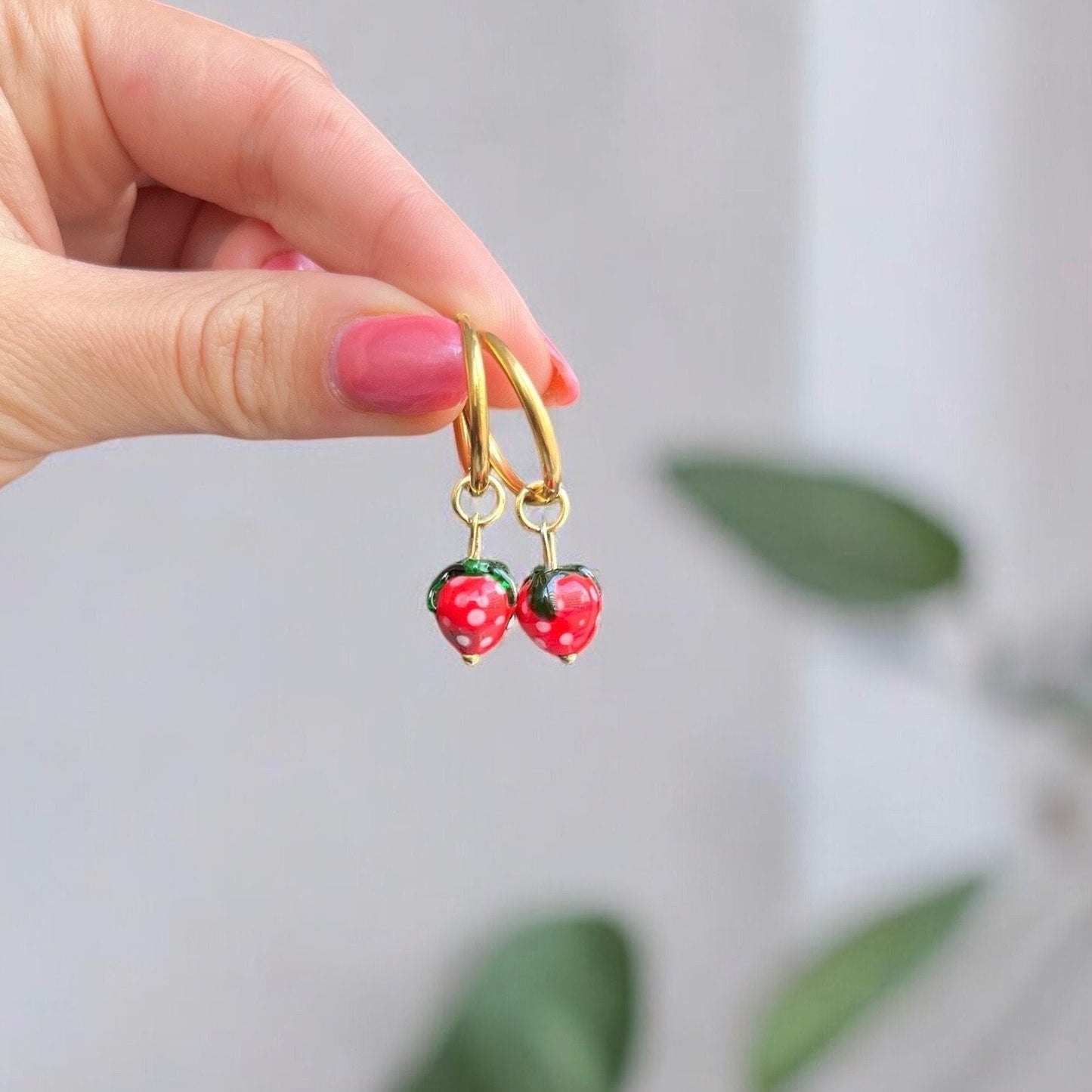 Hand holding a gold hoop earring with strawberry charms against a blurred background