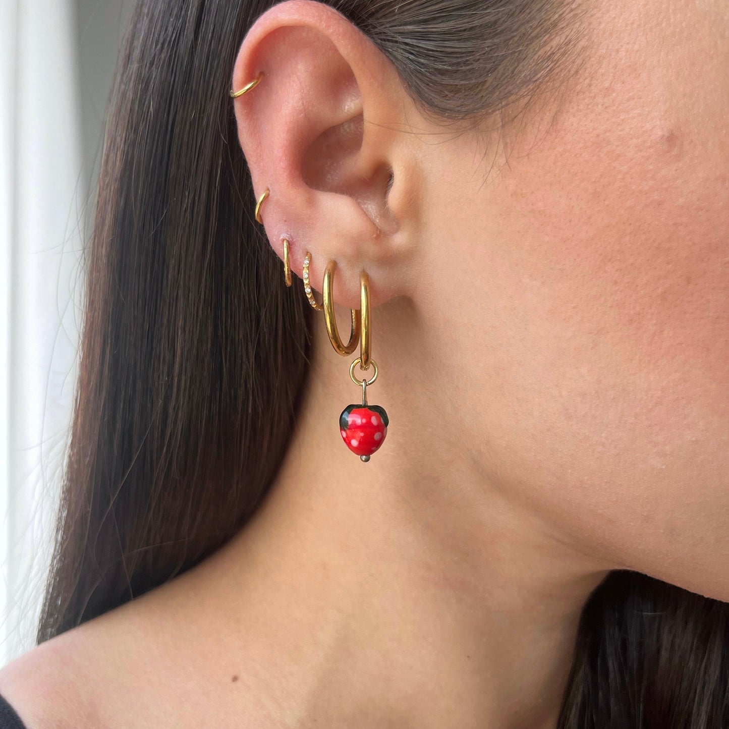 Close-up of a person wearing gold hoop earrings with red ladybug charms.