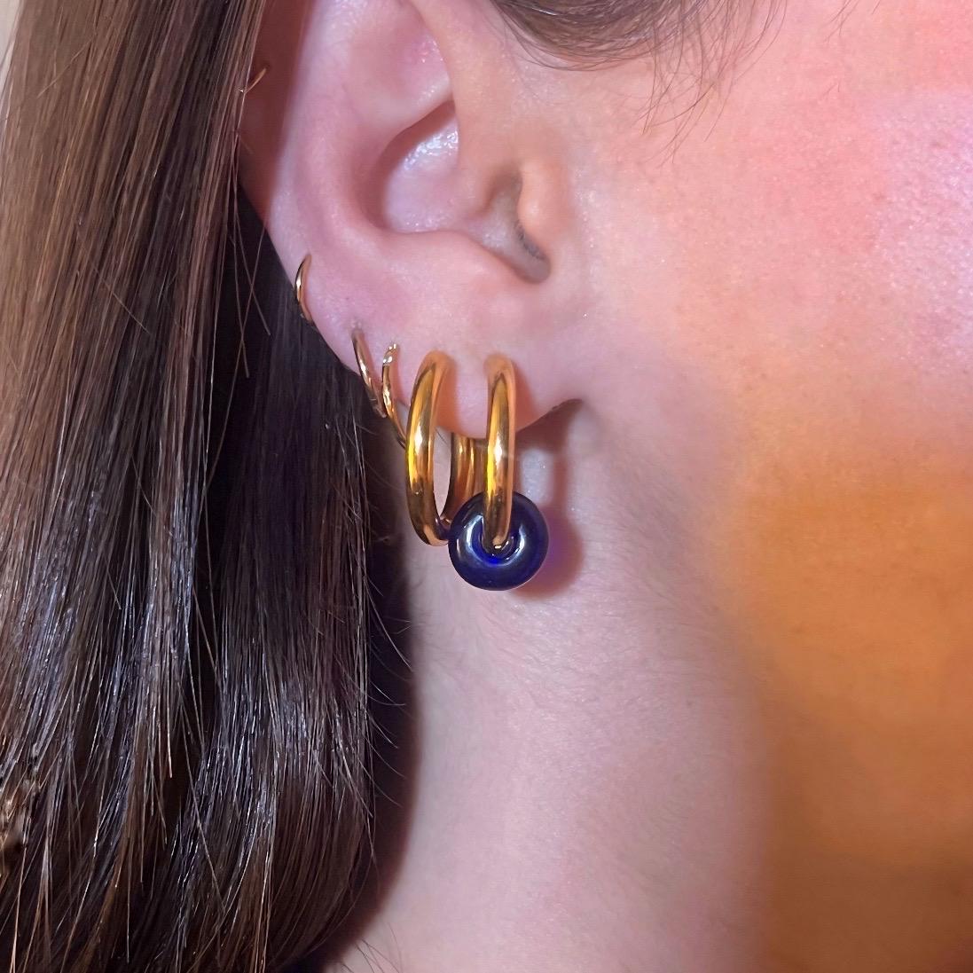 Close-up of an ear wearing a gold hoop earring with a blue gemstone.