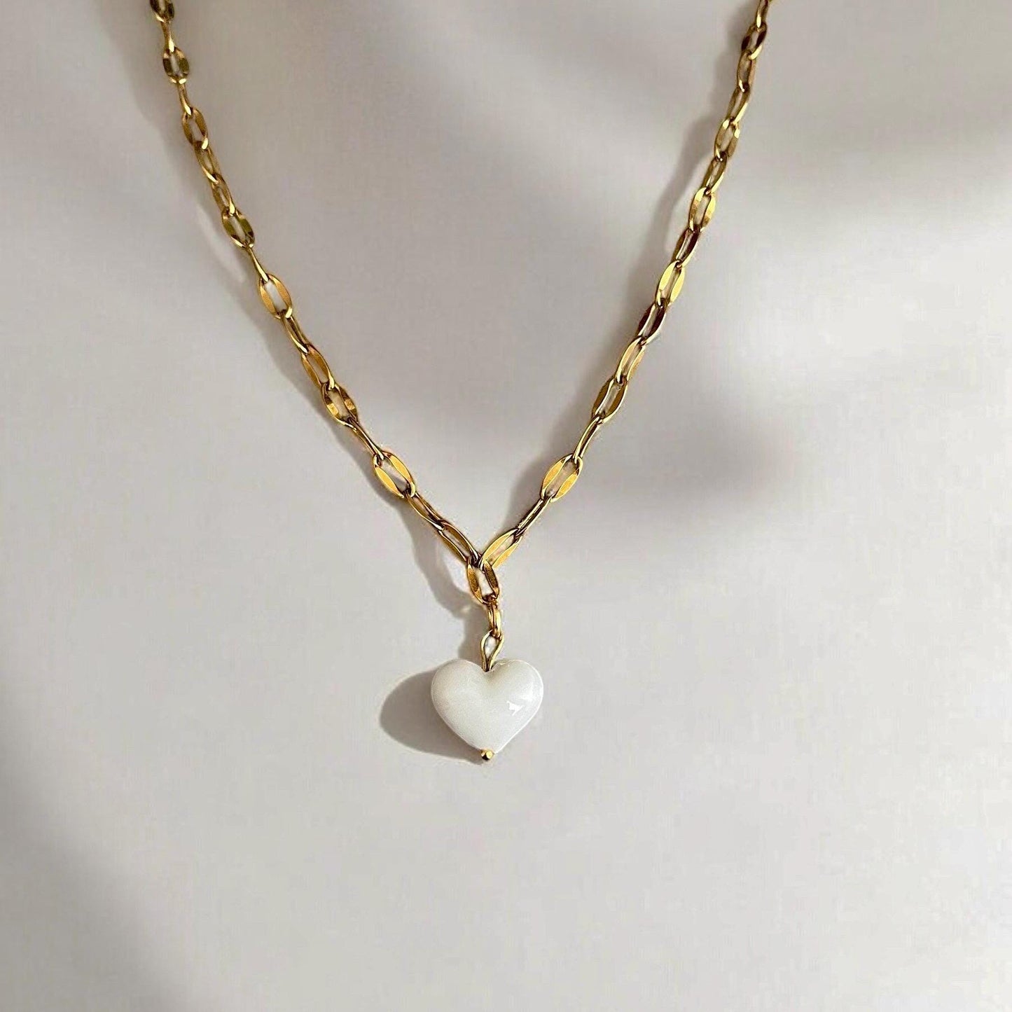 
                  
                    Gold chain necklace with a heart-shaped pendant on a light gray background
                  
                