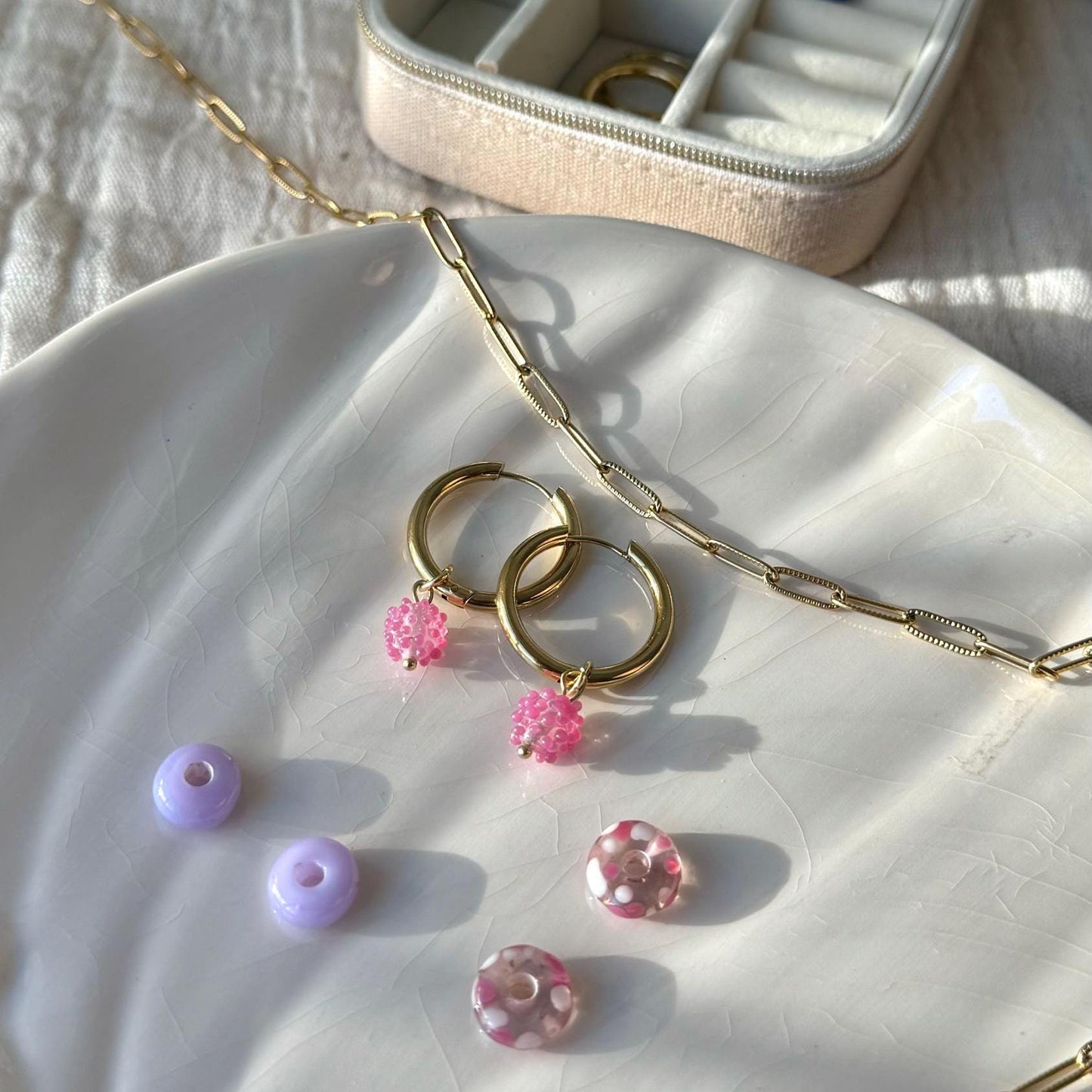 
                  
                    Gold necklace with pink and purple beads on a white surface
                  
                