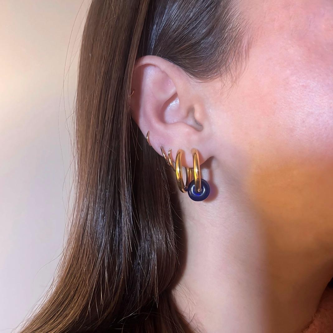 
                  
                    Close-up of an ear wearing gold hoop earrings with a blue center.
                  
                