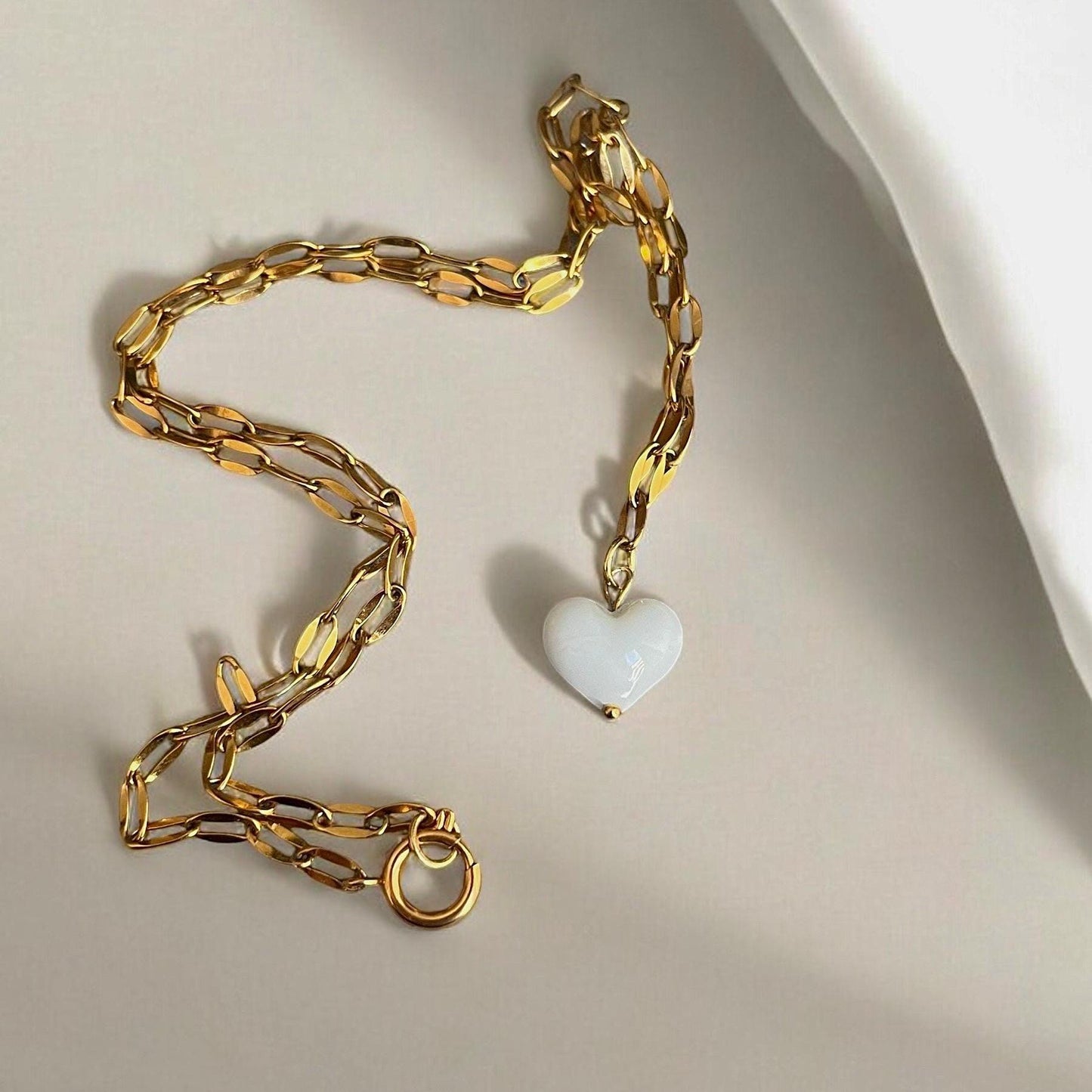 Gold chain necklace with a heart-shaped pendant on a light background