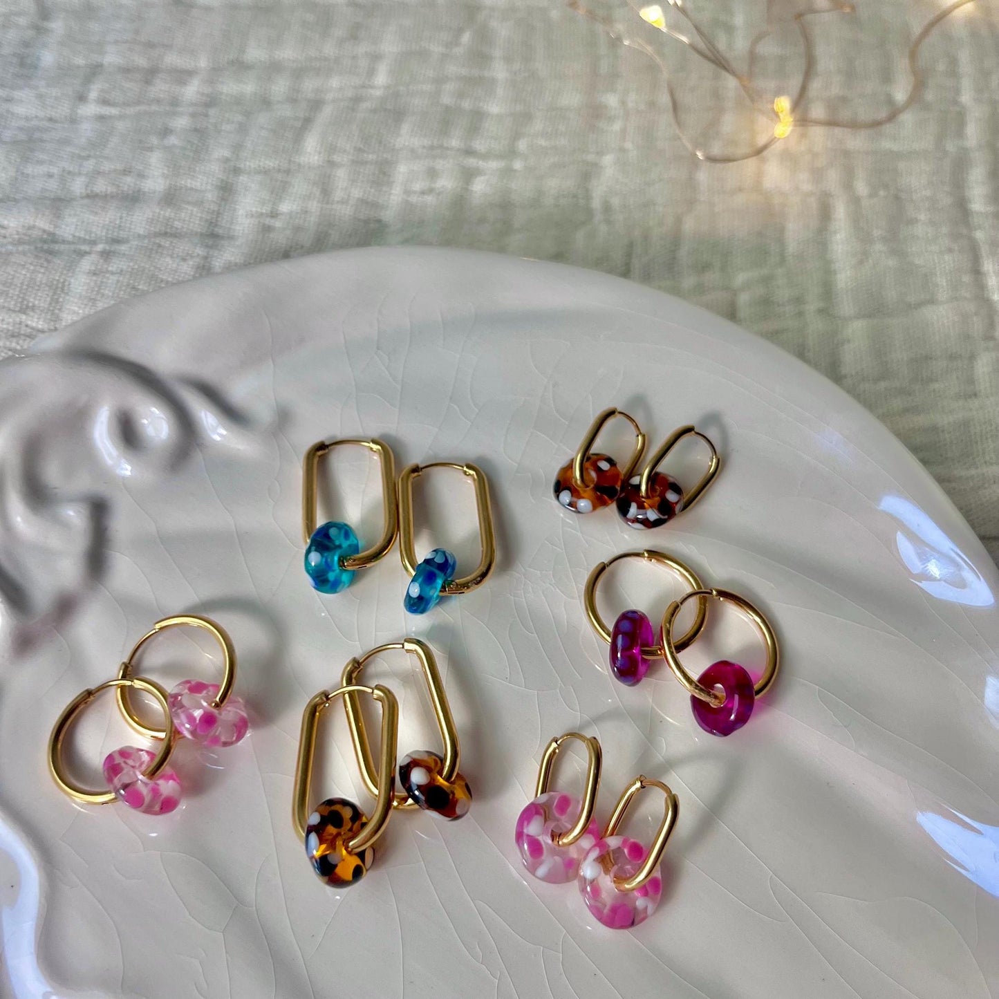 
                  
                    Gold hoop earrings with colorful beads on a white plate.
                  
                