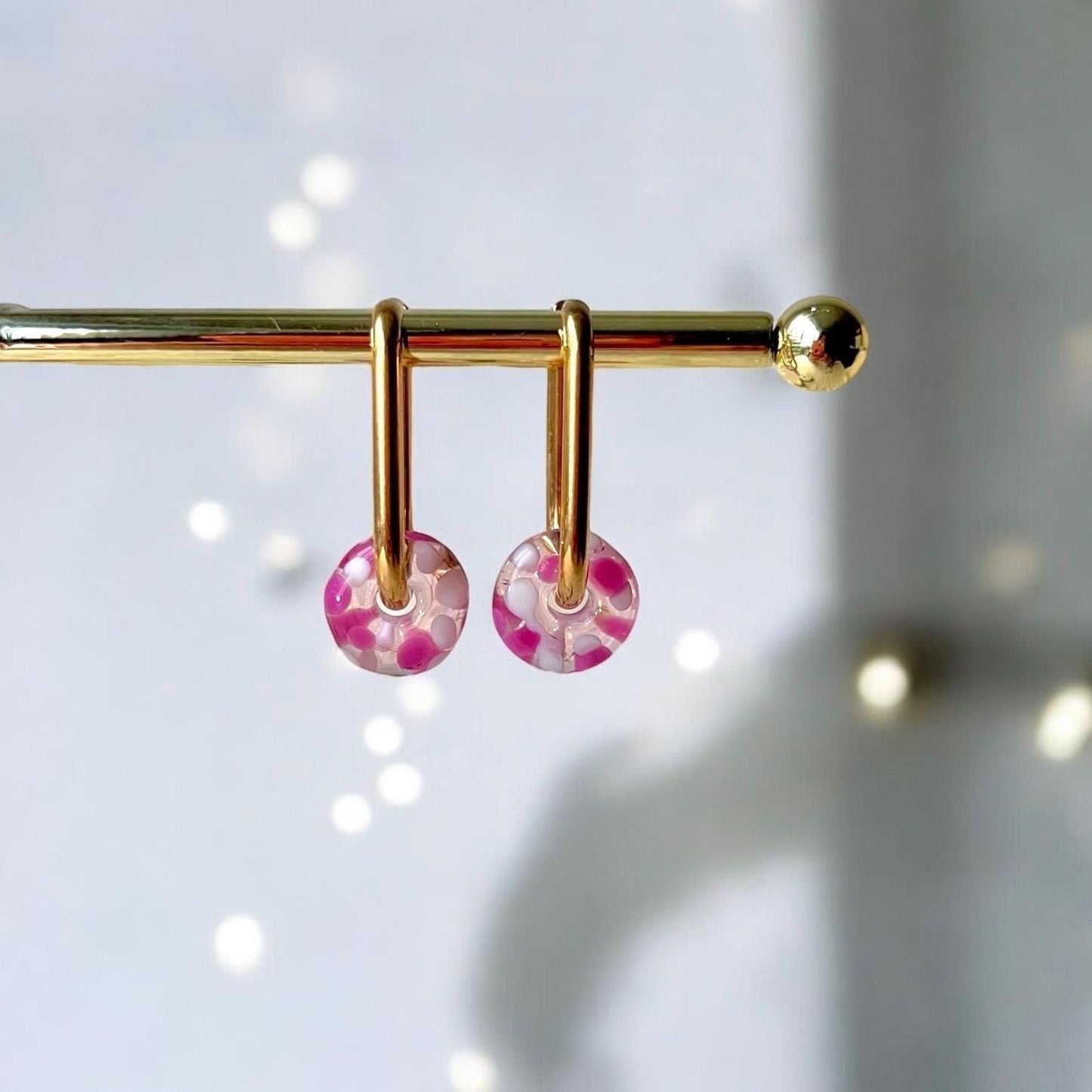 Gold earring with pink floral beads on a white background