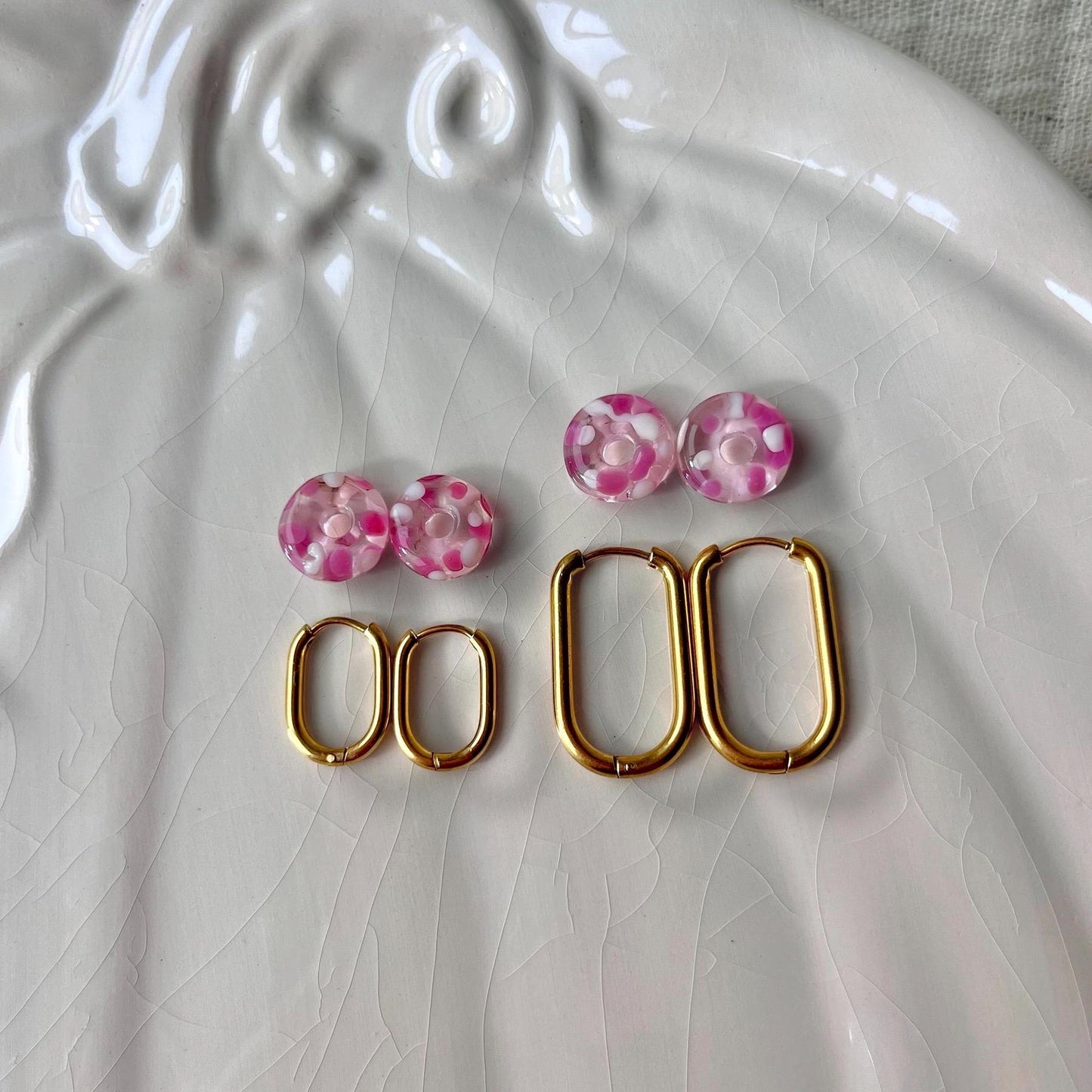 
                  
                    Pair of pink floral earrings with gold hoop earrings on a white textured surface
                  
                
