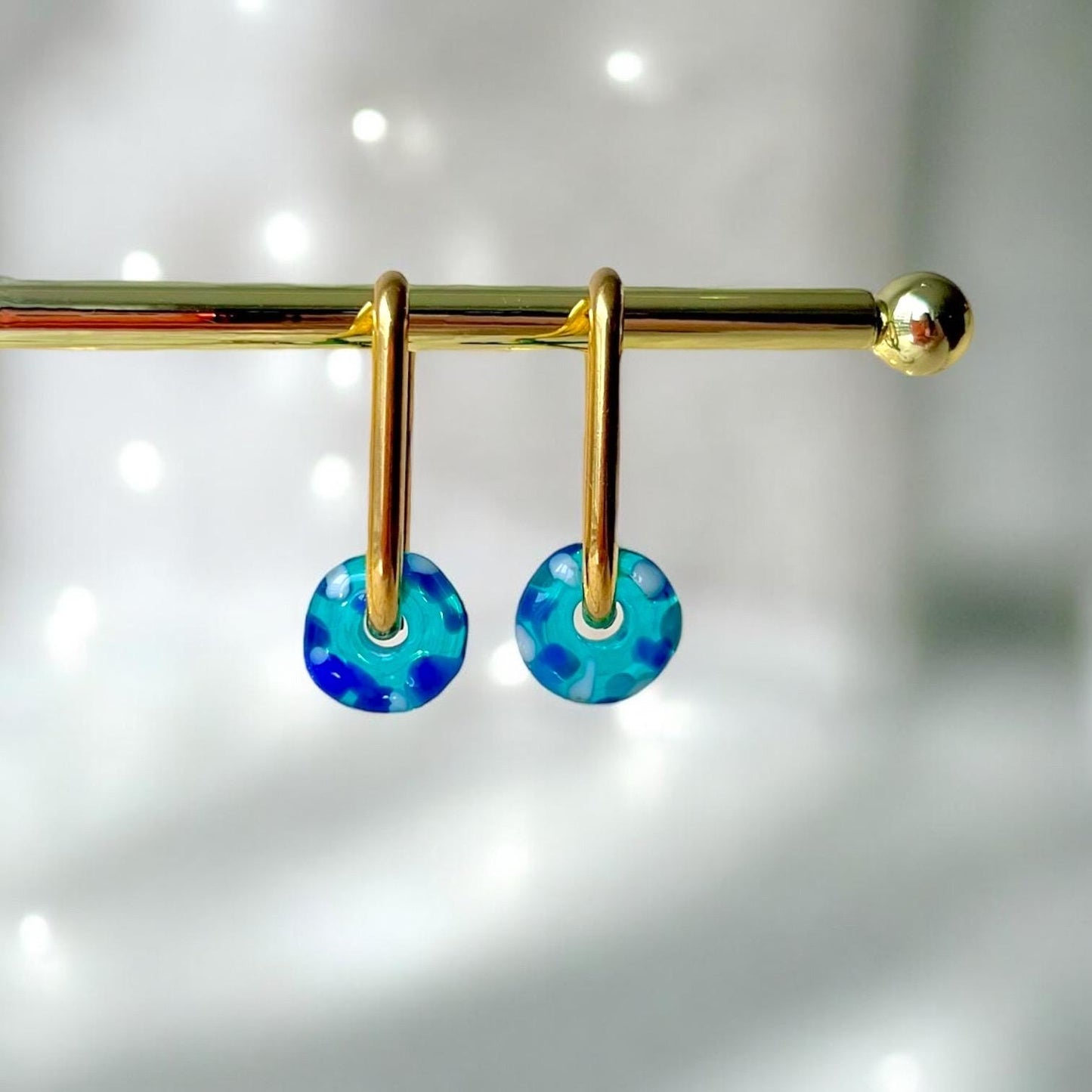 
                  
                    Gold earring with blue and green speckled drops on a white background
                  
                