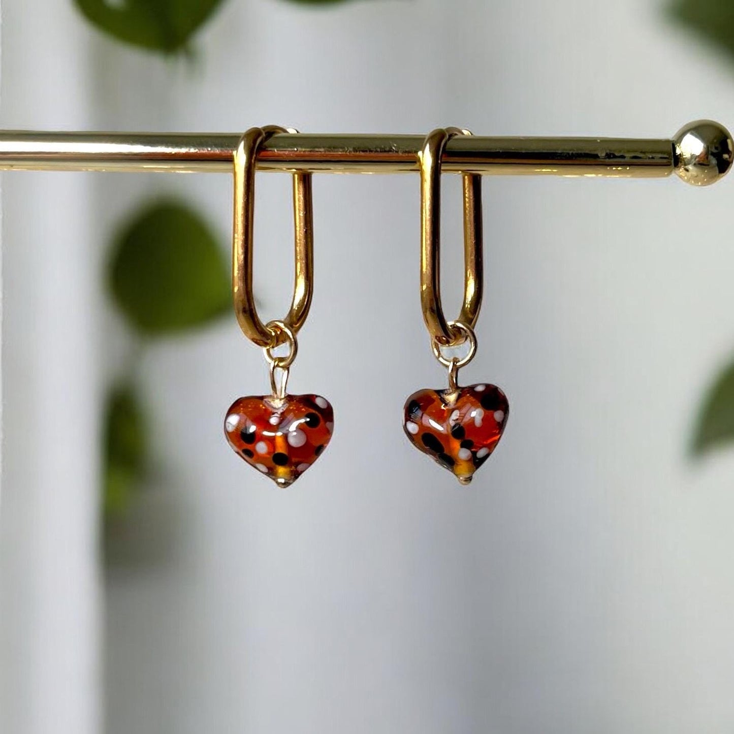 
                  
                    Gold hoop earrings with heart-shaped tortoiseshell charms on a white background
                  
                