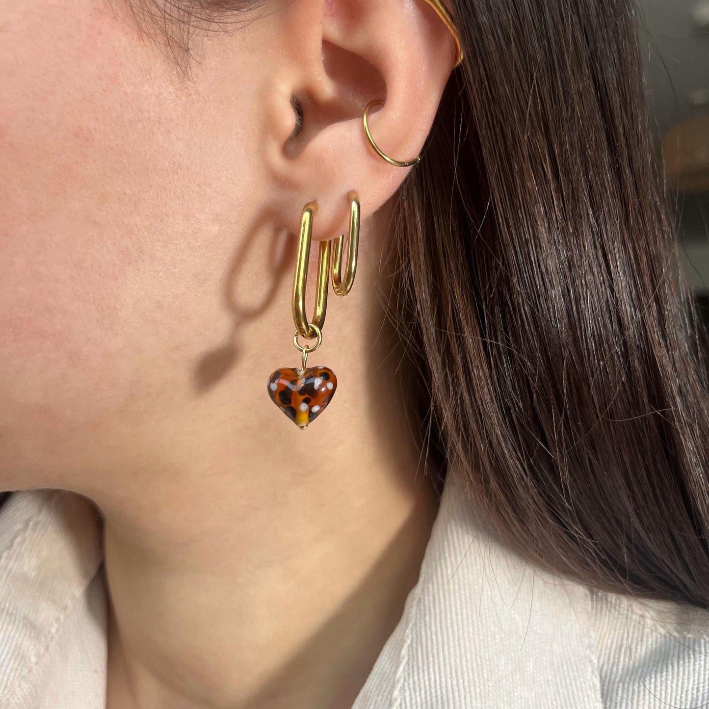 
                  
                    Close-up of a person wearing gold hoop earrings with a tortoiseshell heart charm.
                  
                