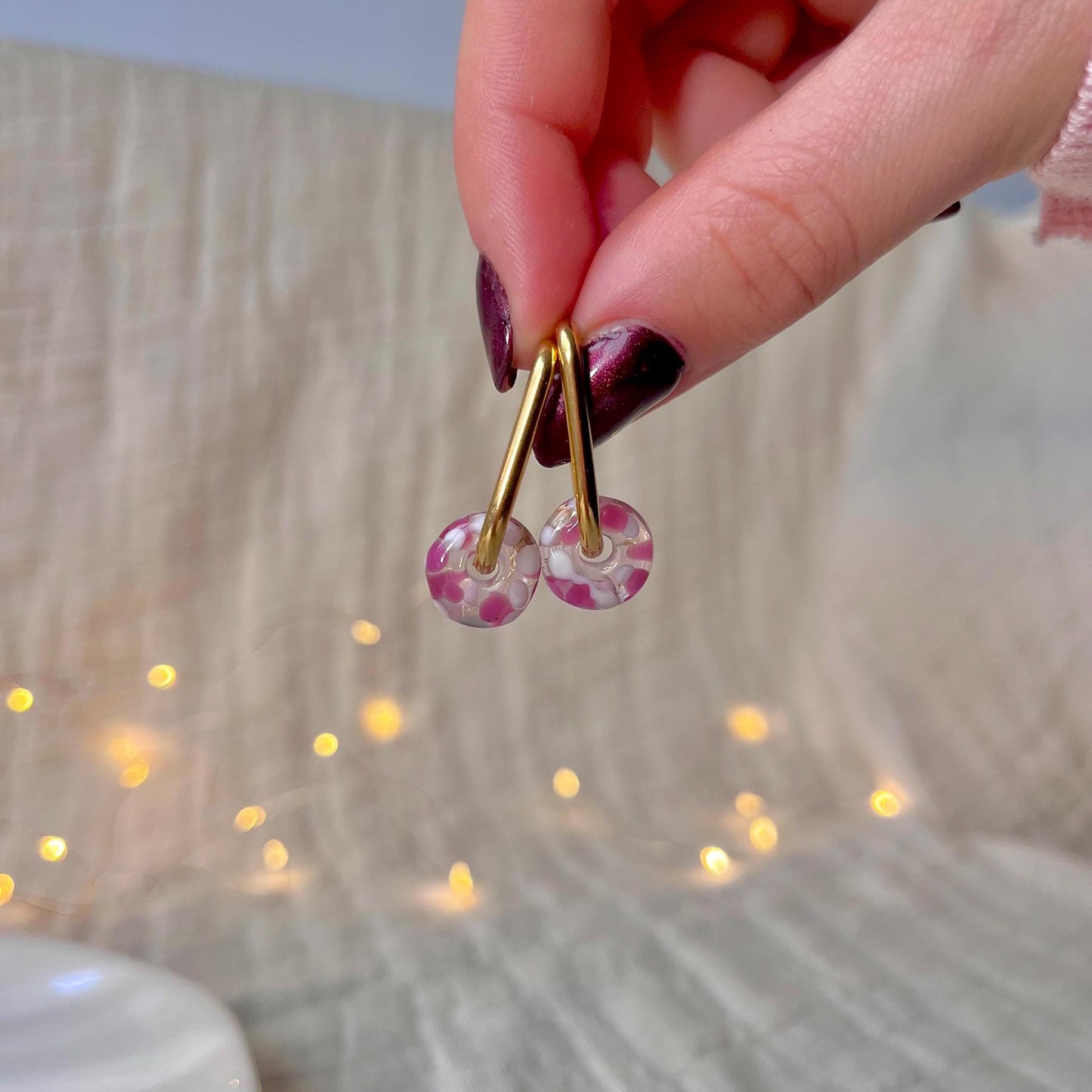 
                  
                    Hand holding a pair of earrings with pink beads against a soft focus background
                  
                