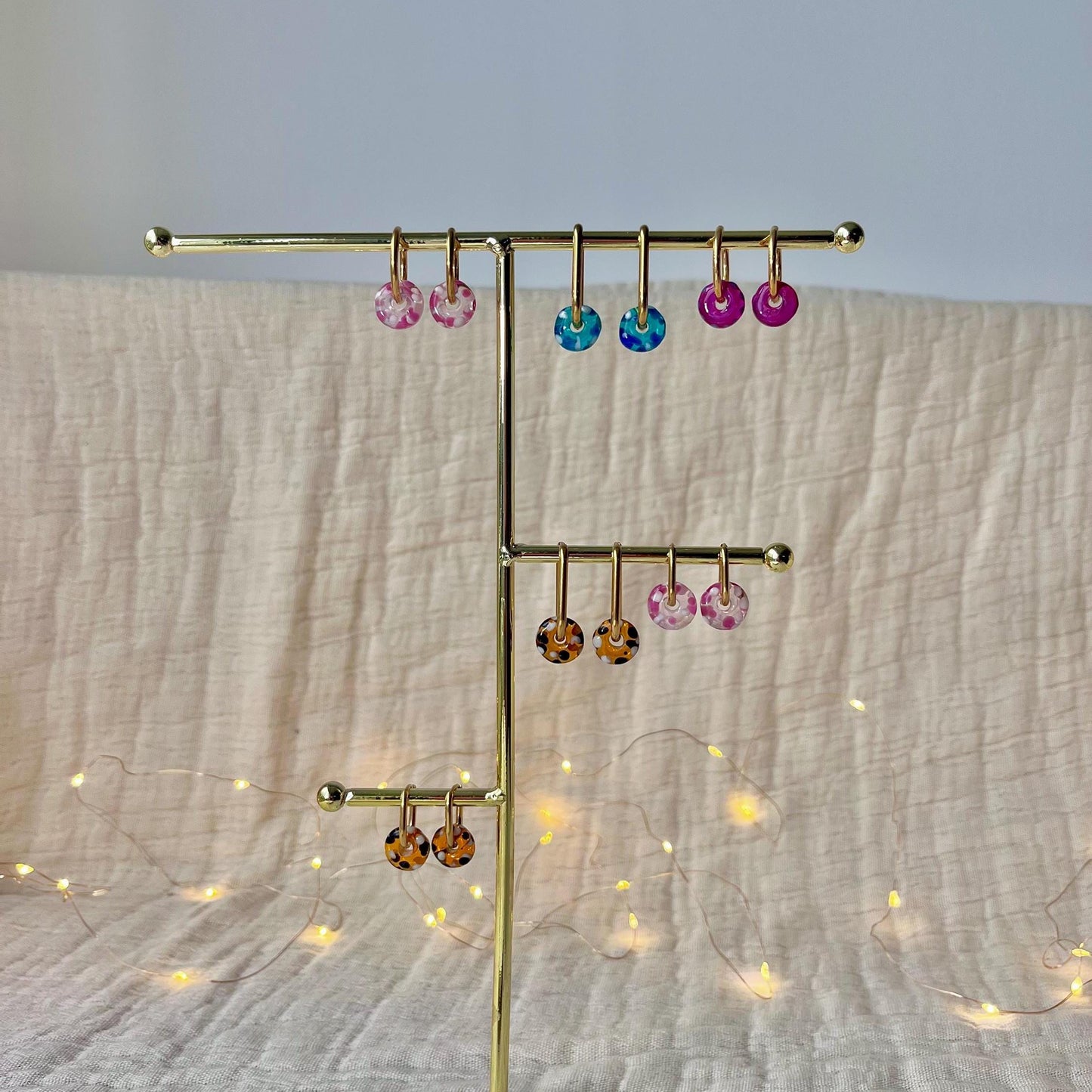 
                  
                    Gold earring stand with colorful earrings on a textured fabric background
                  
                