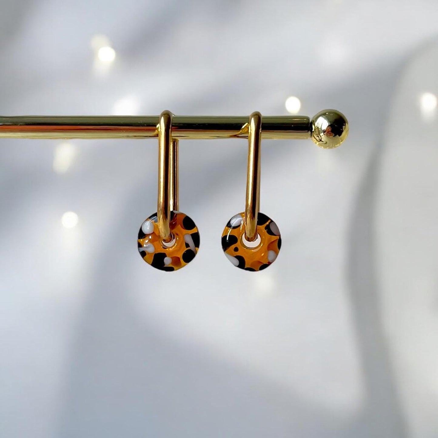 
                  
                    Gold earrings with circular, patterned drops on a light gray background
                  
                