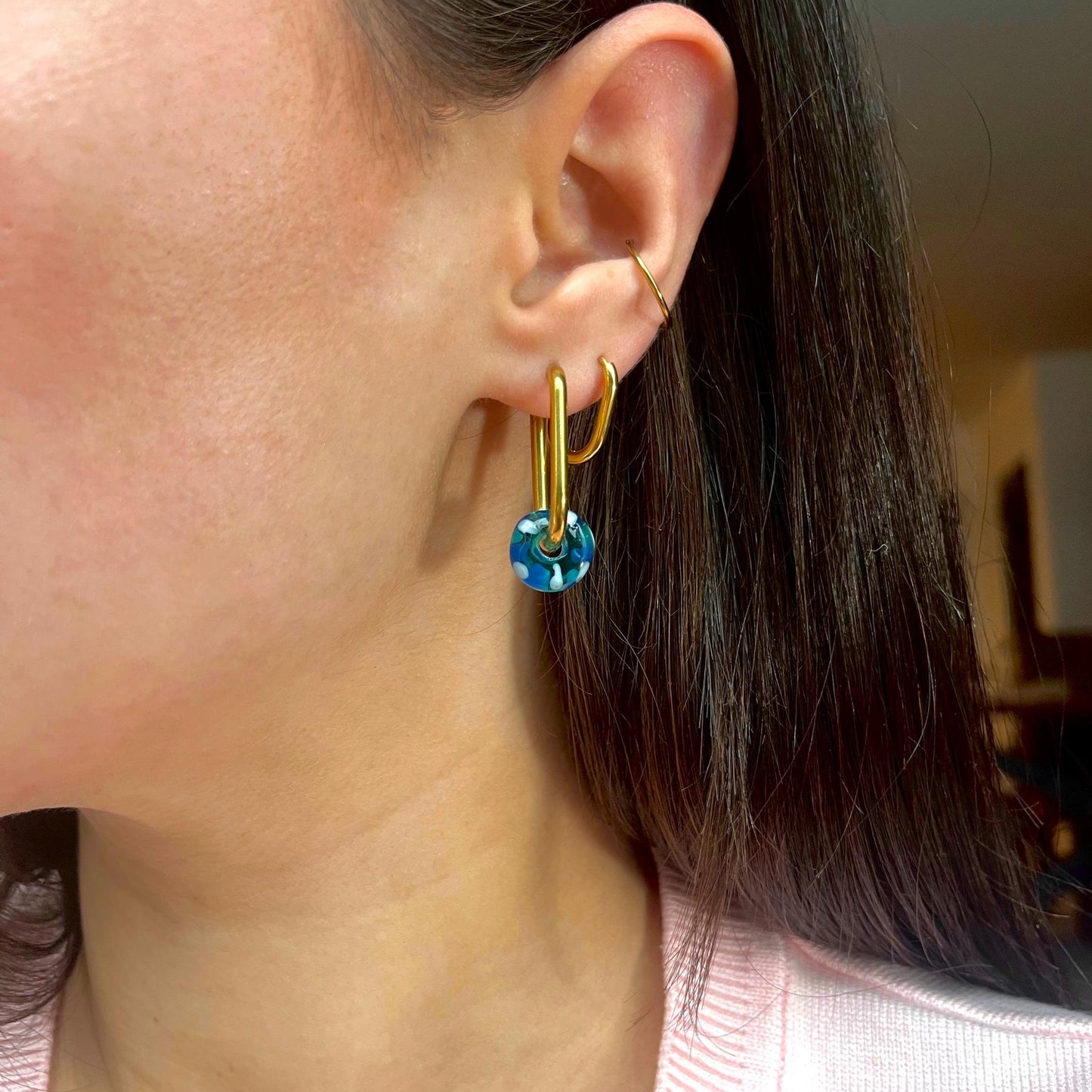 
                  
                    Close-up of a person wearing gold hoop earrings with blue heart charms.
                  
                