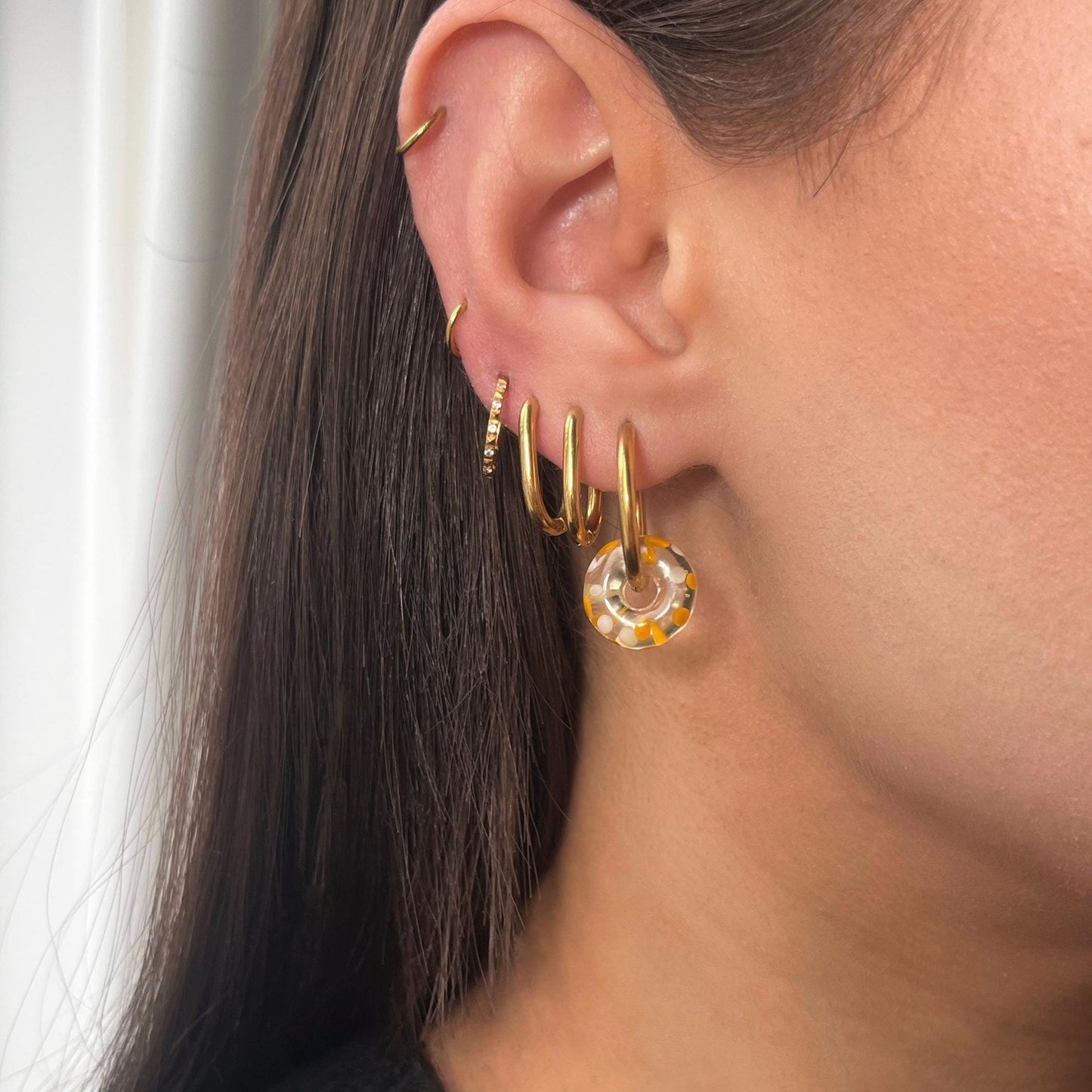 Close-up of an ear wearing gold hoop earrings with a clear gemstone.