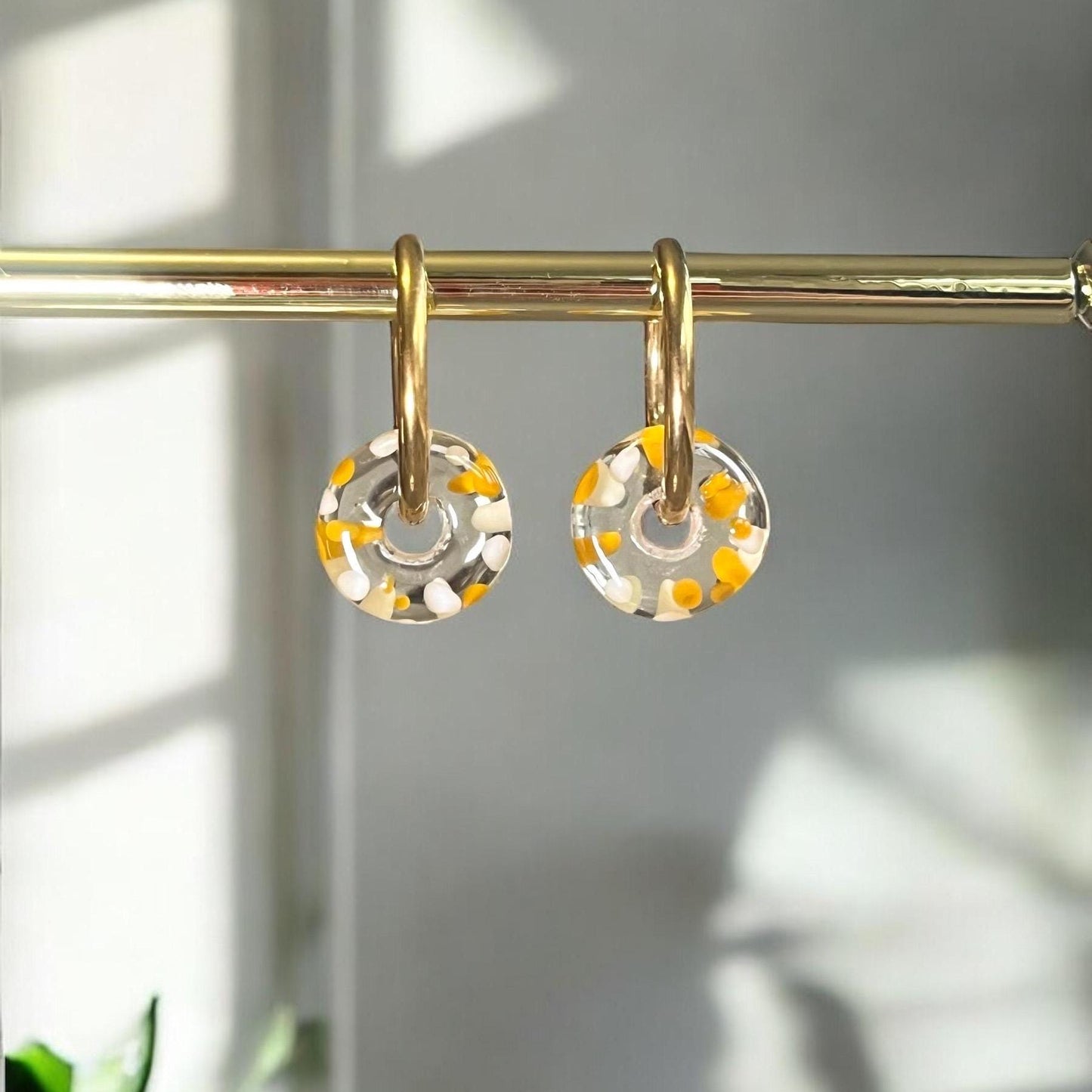 
                  
                    Gold hoop earrings with circular clear stones featuring orange and white patterns on a light background.
                  
                