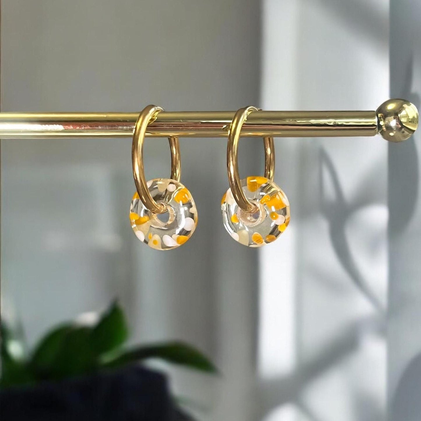 Gold shower curtain rings with clear and orange floral designs on a gold rod against a neutral background.