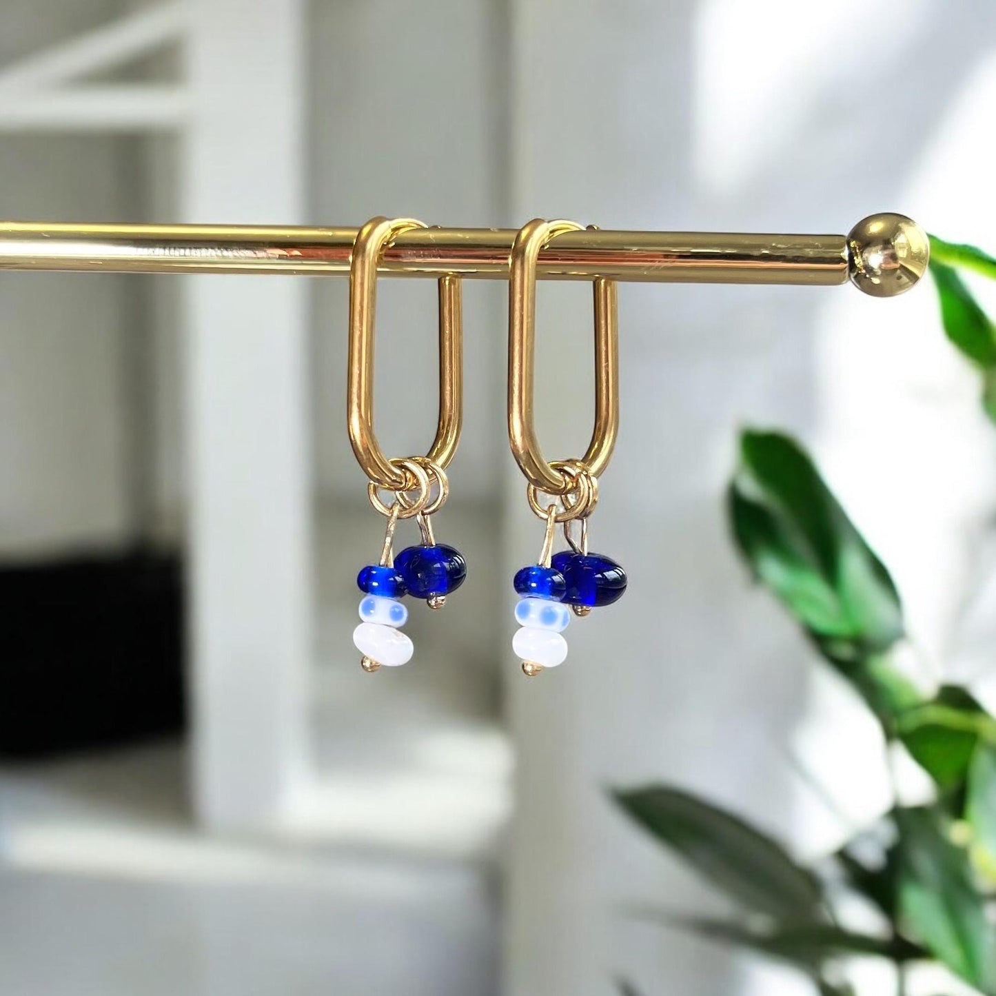 
                  
                    Gold earrings with blue and white beads on a gold stand against a blurred background
                  
                