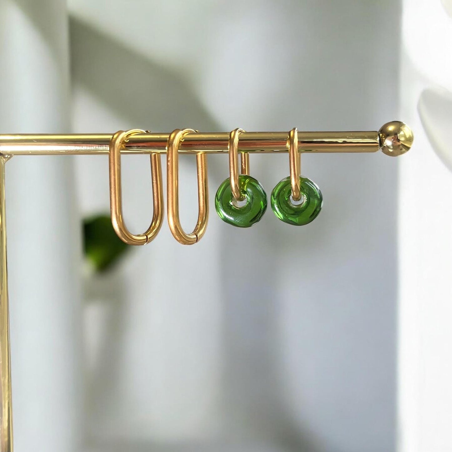 Gold hooks with green circular ends hanging on a gold rod against a white background