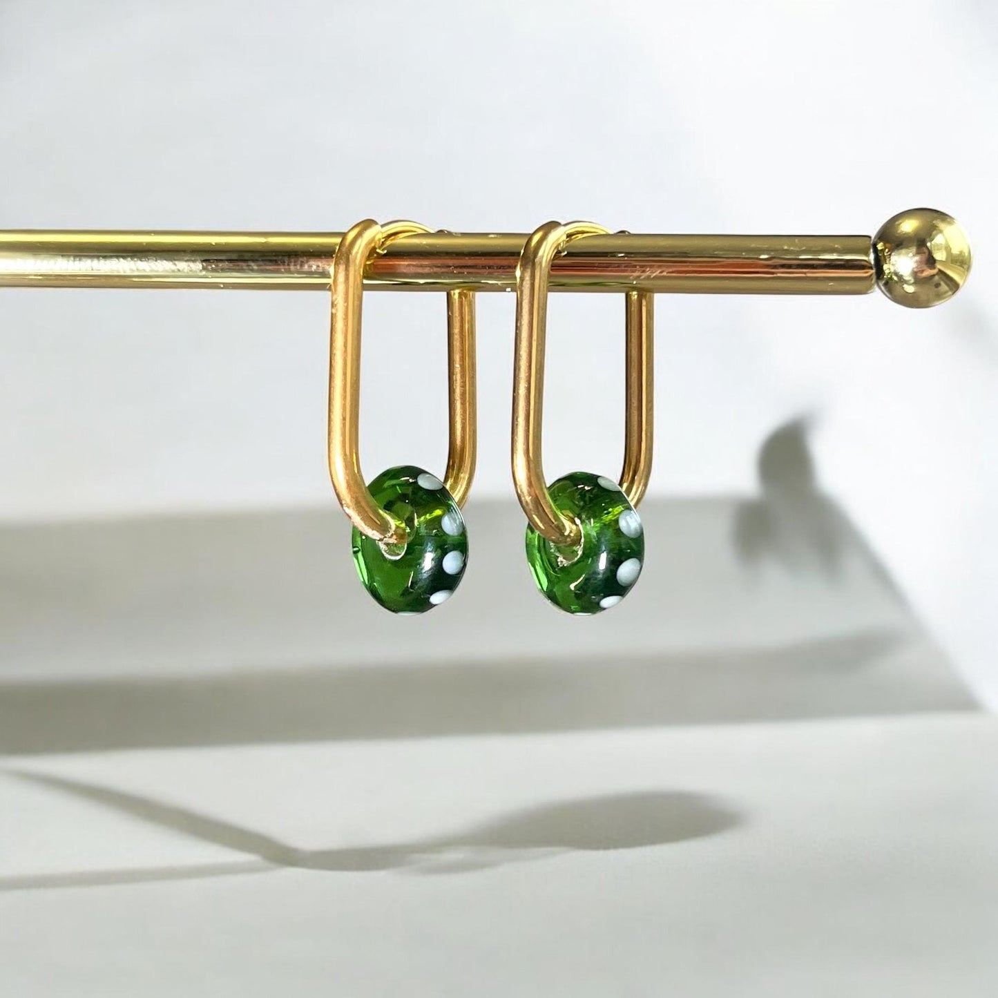 Gold earring hook with green beads on a white background