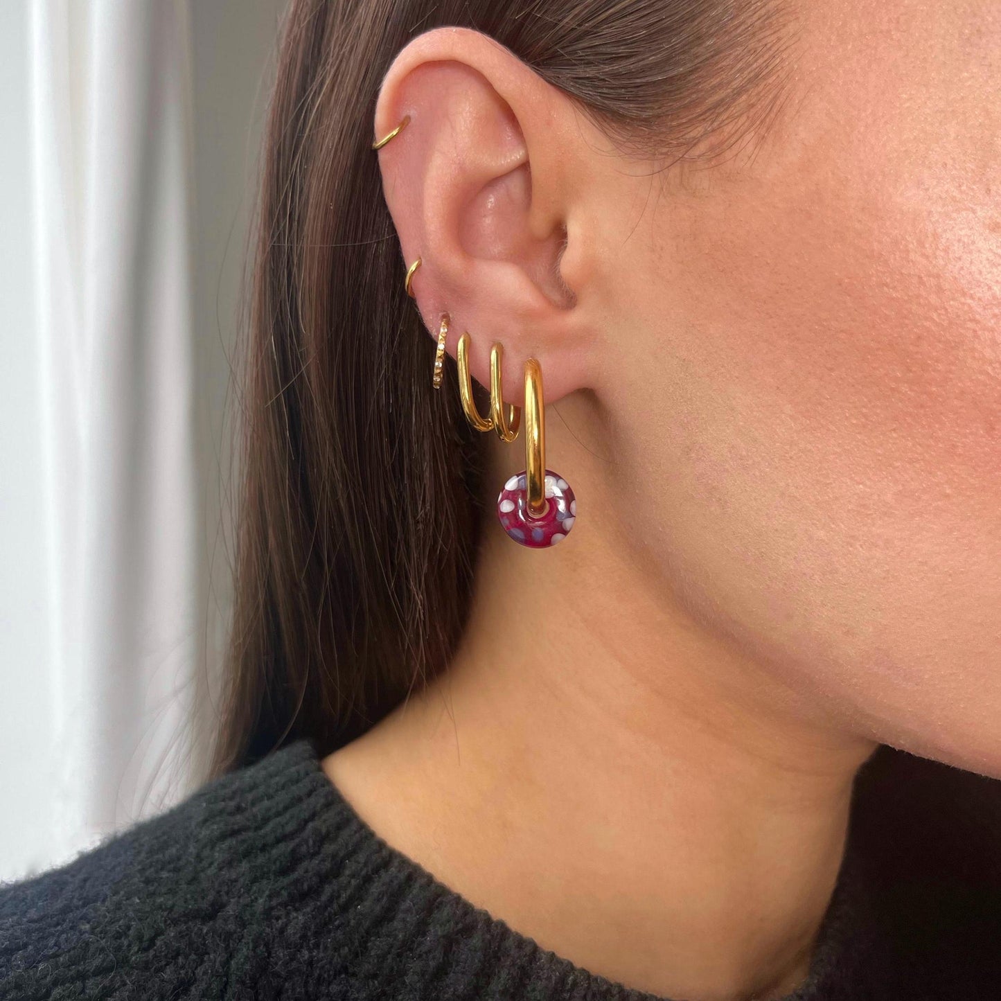 Close-up of an ear with gold hoop earrings and a purple gemstone earring.