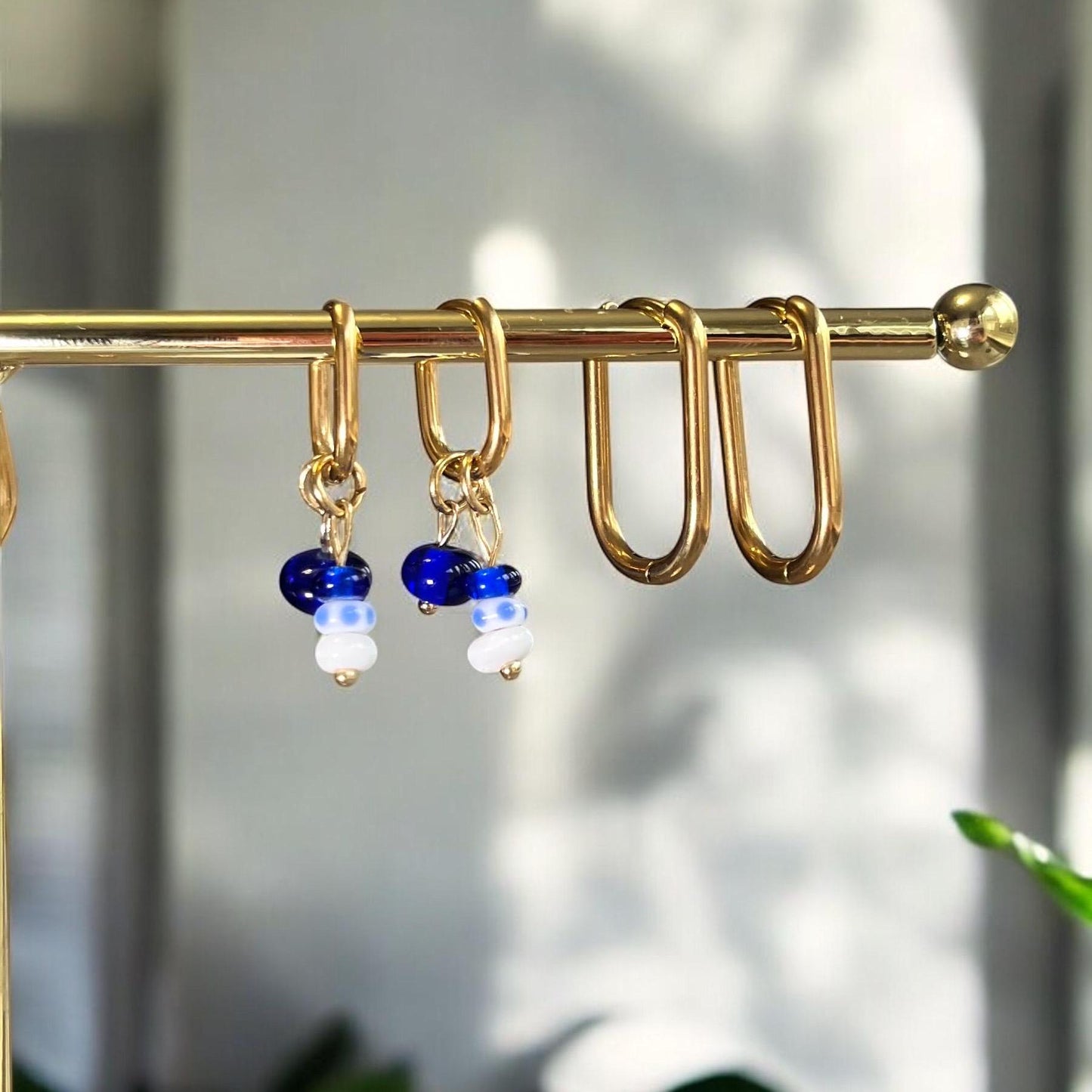 
                  
                    Gold earring hooks with blue and white beads on a gold rod against a blurred natural background.
                  
                