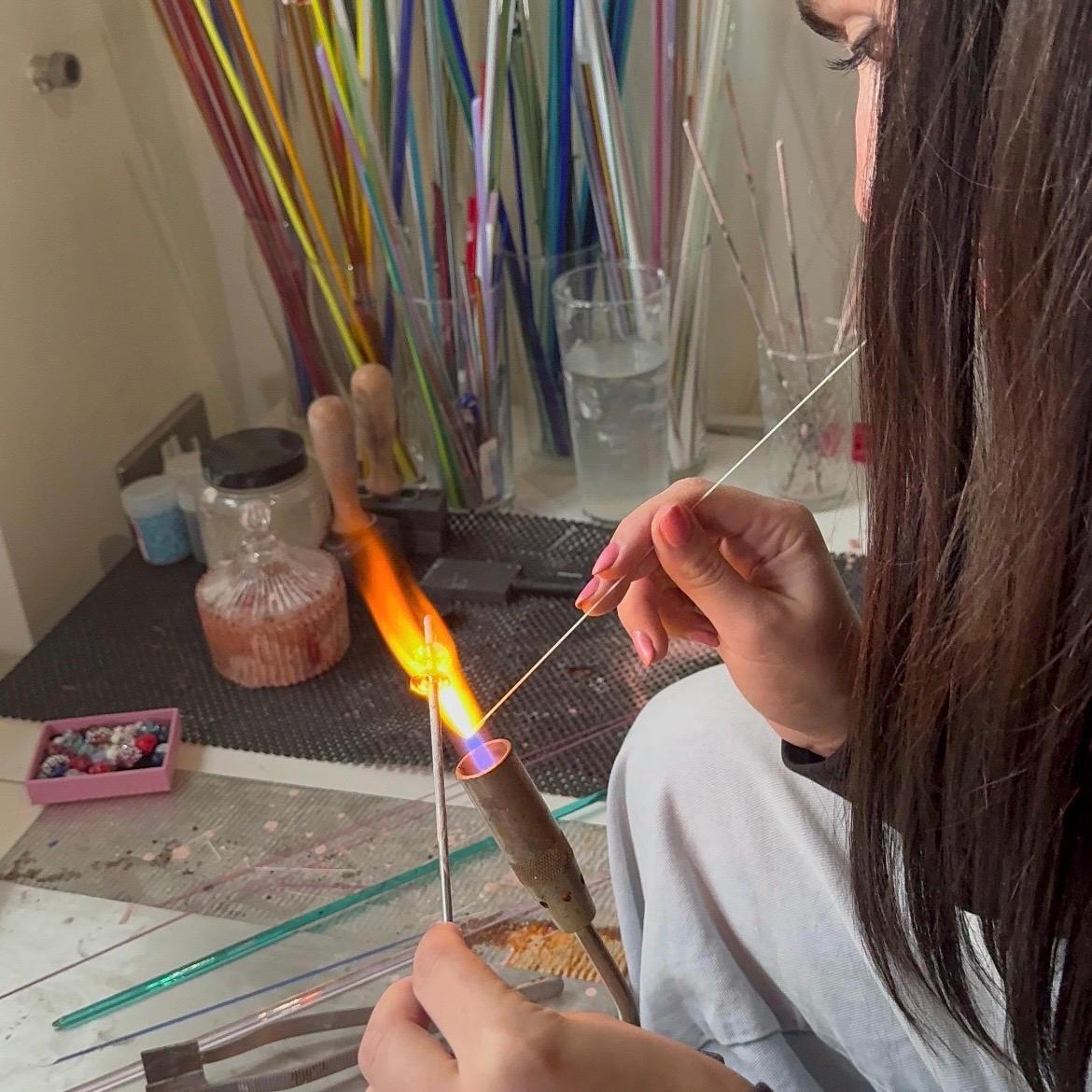 Person working with glassblowing tools and materials in a workshop setting.
