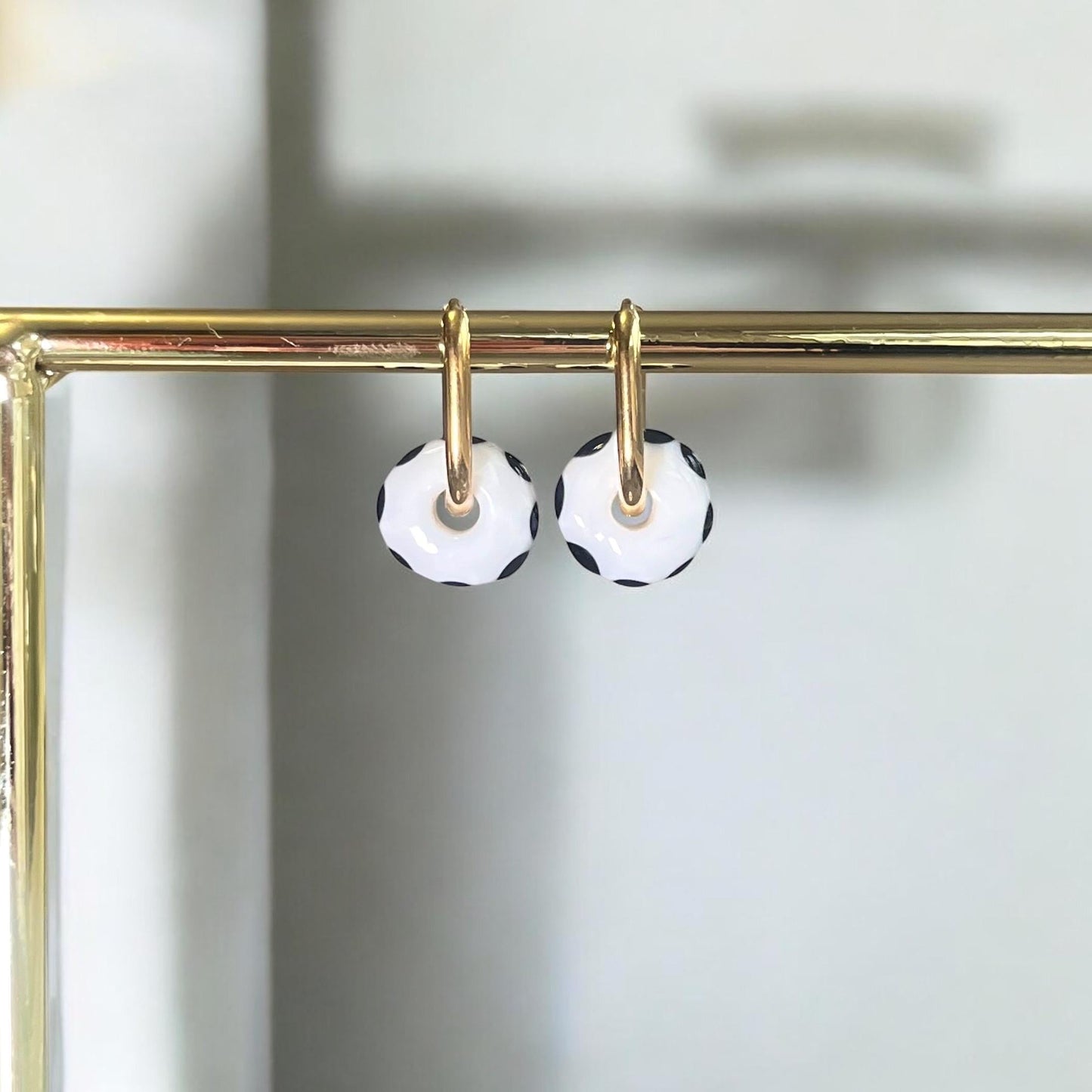 
                  
                    Black and white polka dot earrings on a gold hoop against a neutral background
                  
                