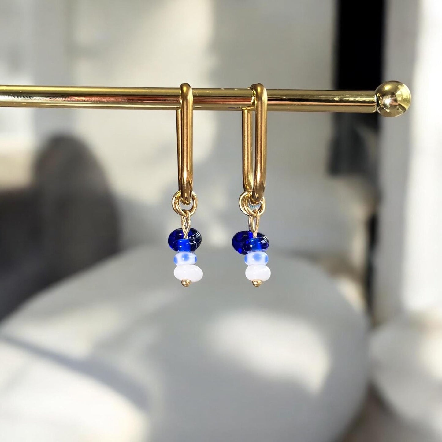 Gold earrings with blue and white beads on a blurred background