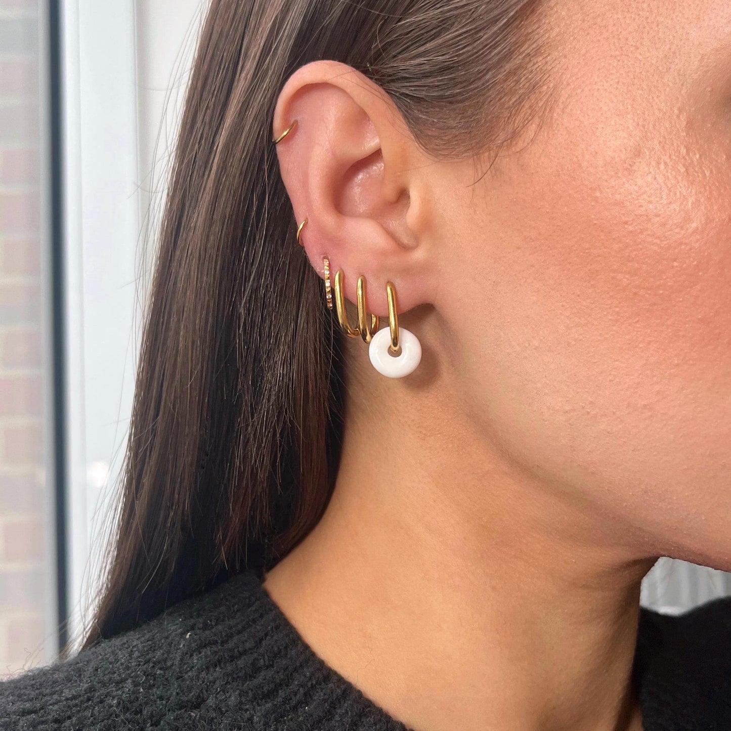 Close-up of a person wearing gold hoop earrings with white stones.