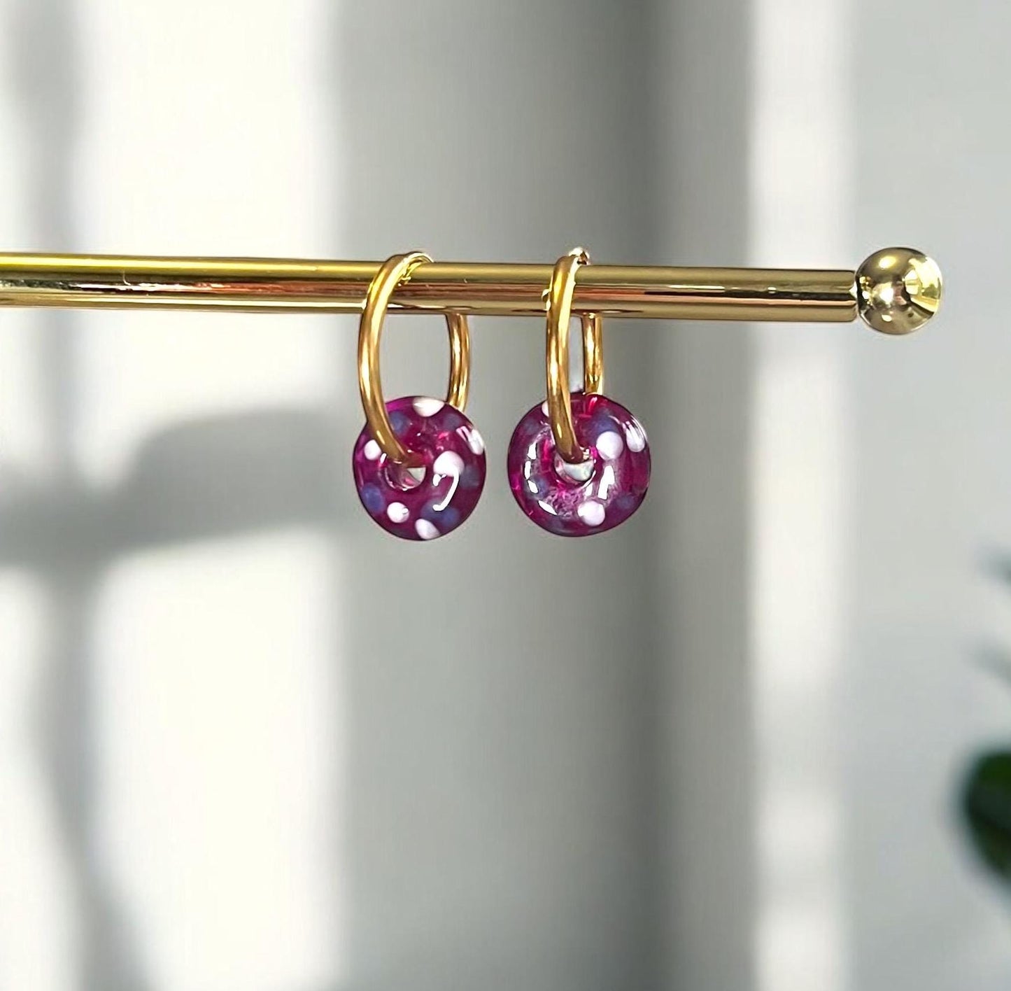 
                  
                    Gold hoop earrings with pink gemstones on a gold rod against a neutral background
                  
                