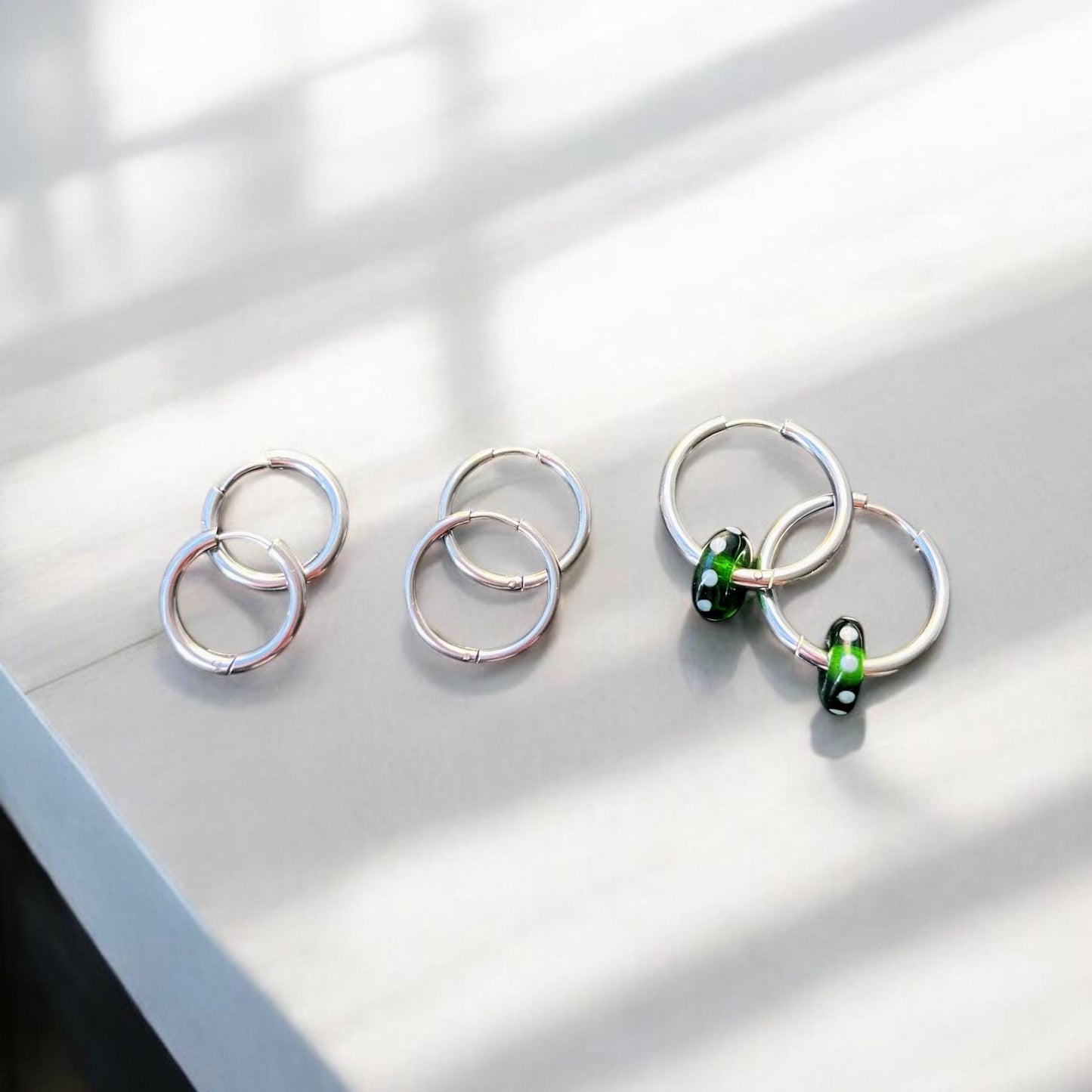 
                  
                    Silver ring earrings with green beads on a light surface
                  
                
