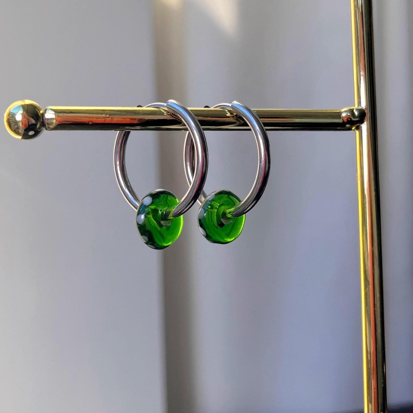 Silver hoop earrings with green beads on a gold stand against a neutral background