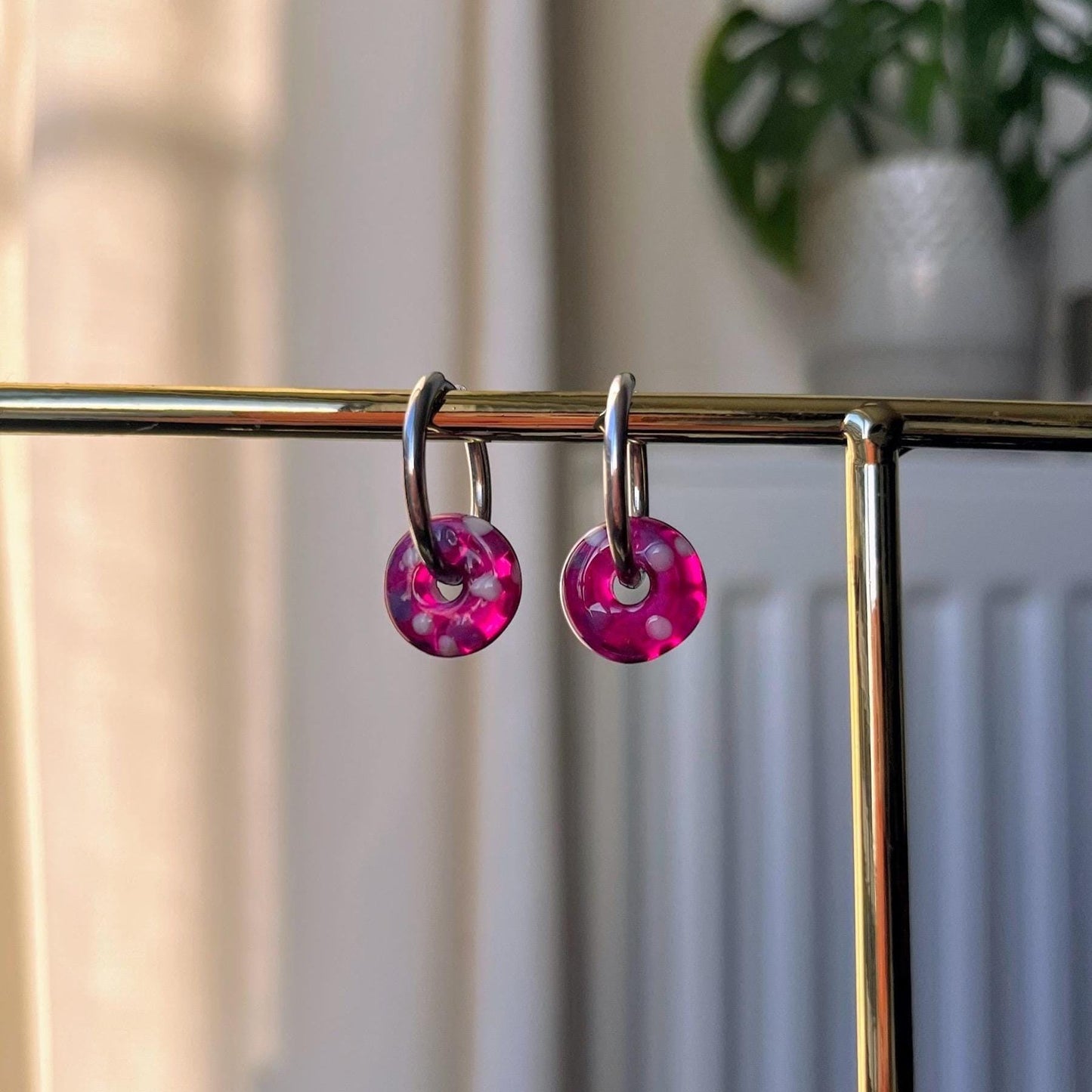 Pink earrings hanging on a gold rack with a blurred indoor background