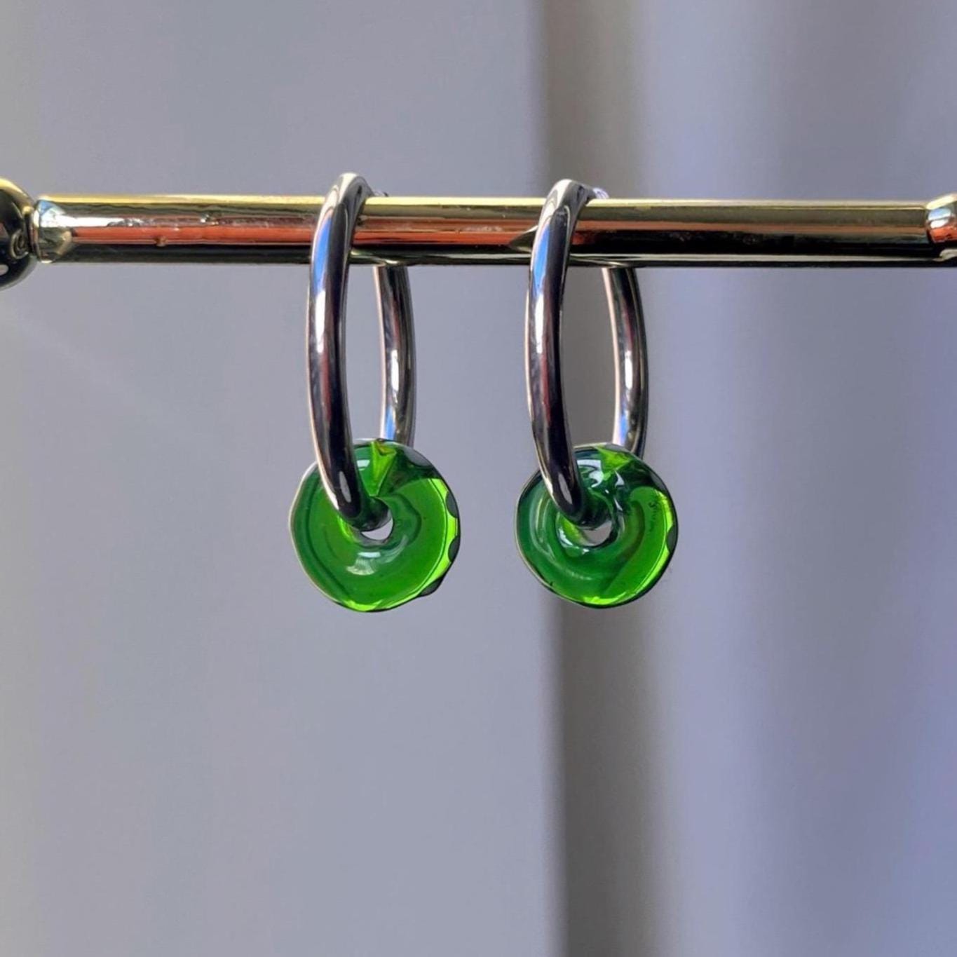 Silver hoop earrings with green circular charms on a gray background