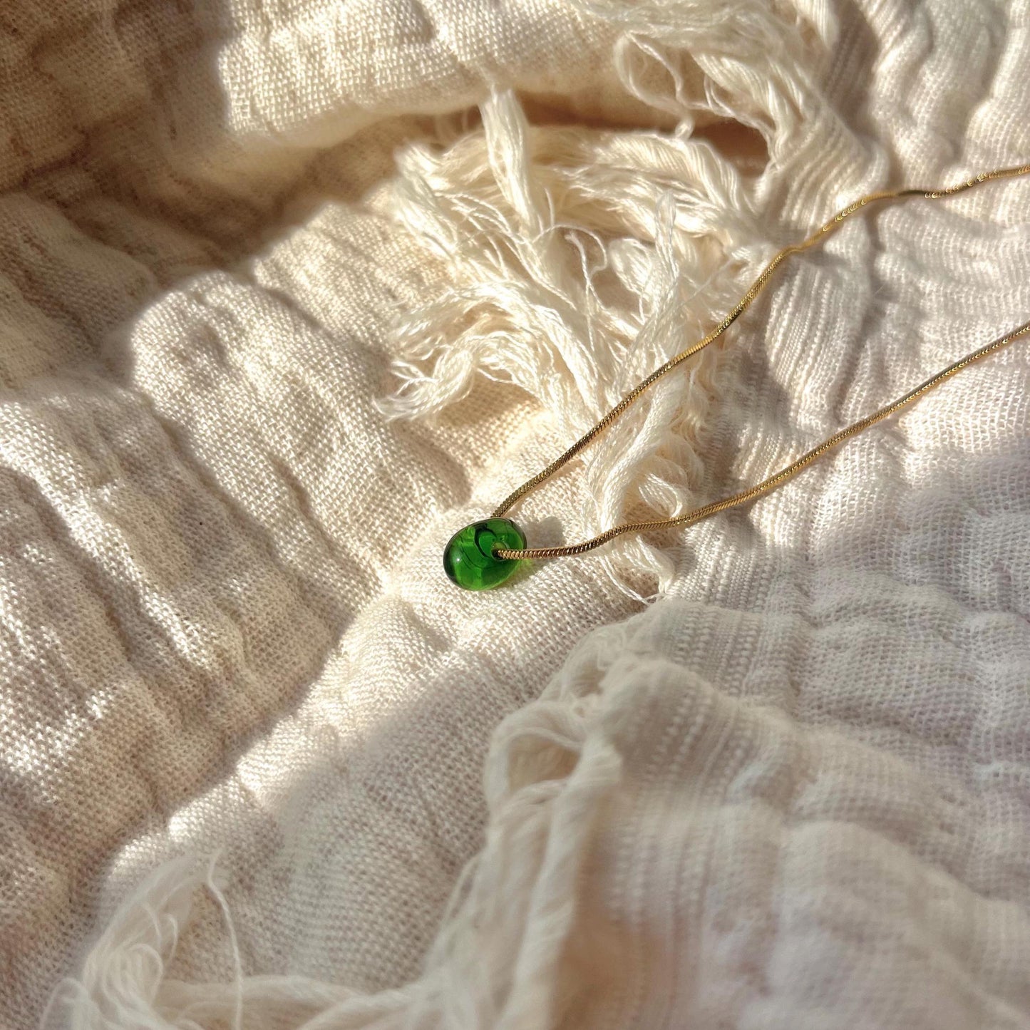 
                  
                    Necklace with a green pendant on a textured white fabric background
                  
                